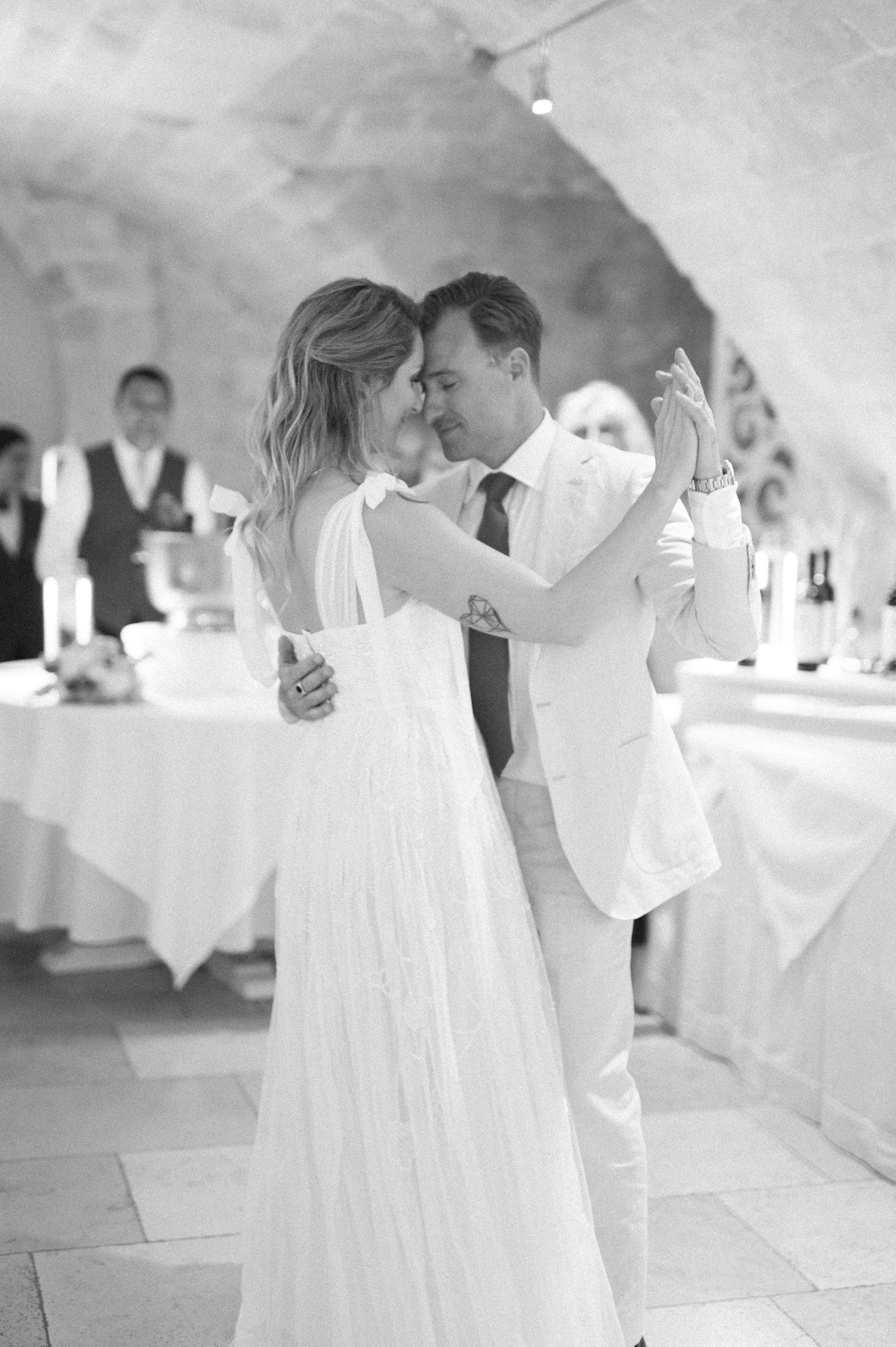 Dancing couple in formal attire twirling across a white-decorated reception venue.