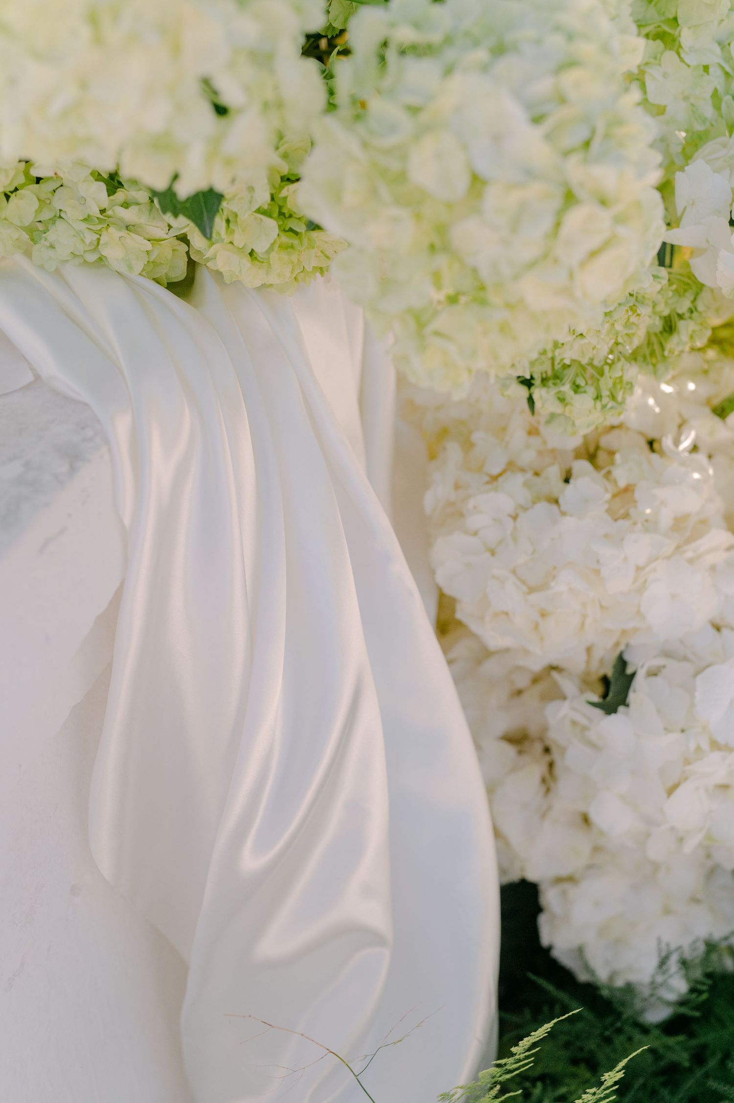 Elegant white hydrangea floral arrangement with draped silk fabric for a luxurious wedding ceremony decor.