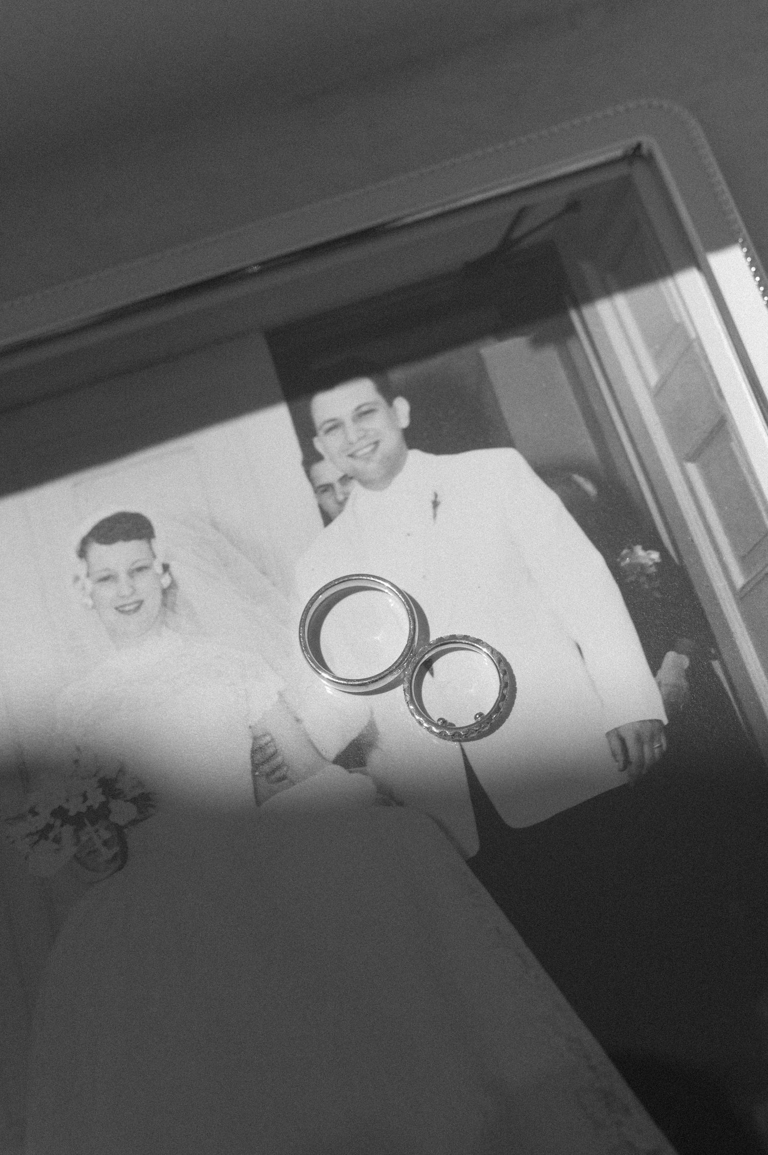 Black and white vintage wedding photo reflected in mirror with two gold wedding rings in foreground.