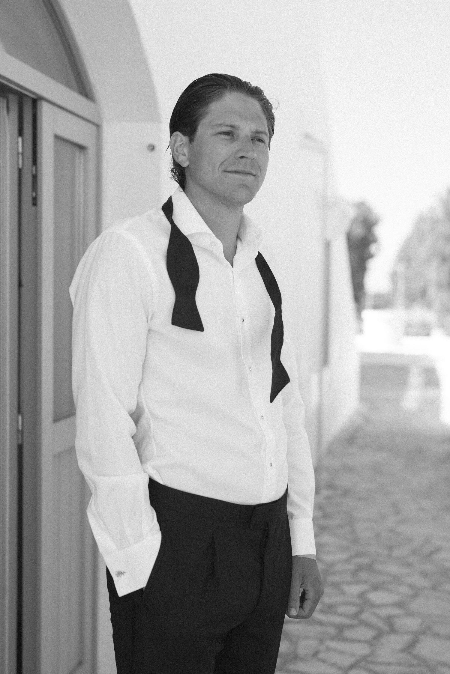 Stylish man in white dress shirt and black vest posing outdoors in black and white photo.