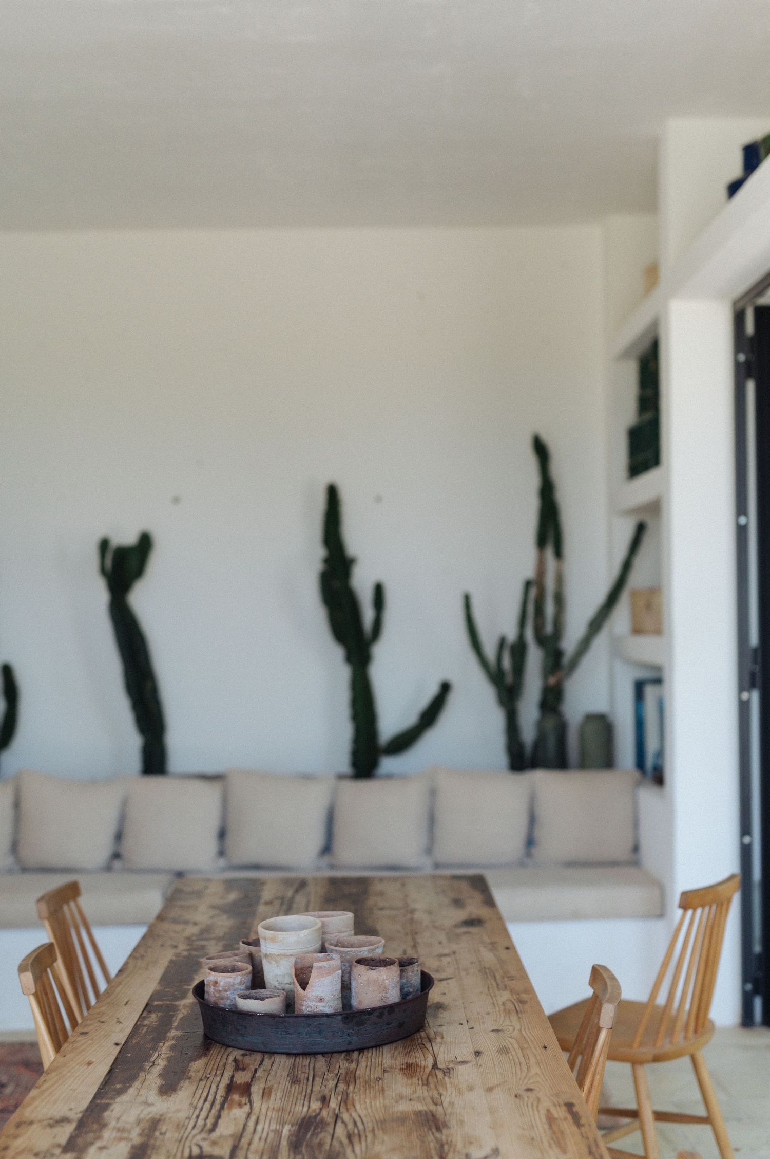 Modern dining room with rustic wooden table, wooden chairs and black cacti silhouettes against white wall.