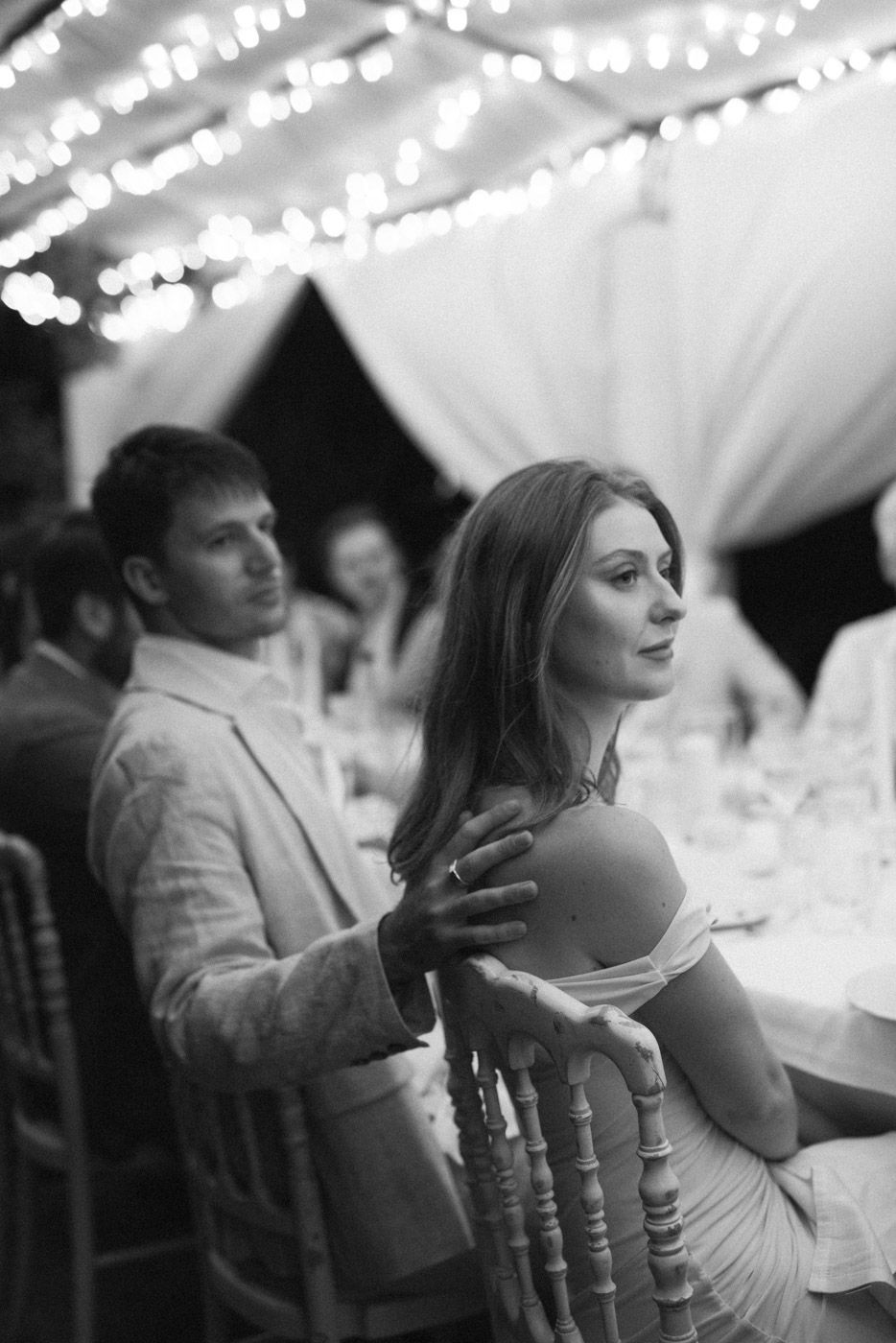 Wedding guests seated at tables under a white tent during an elegant reception.