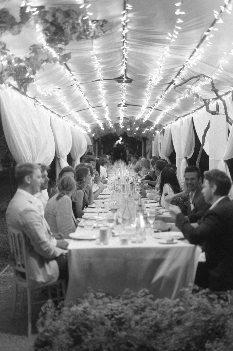 Wedding reception tent decorated with draped fabric and string lights creates an intimate dining atmosphere.