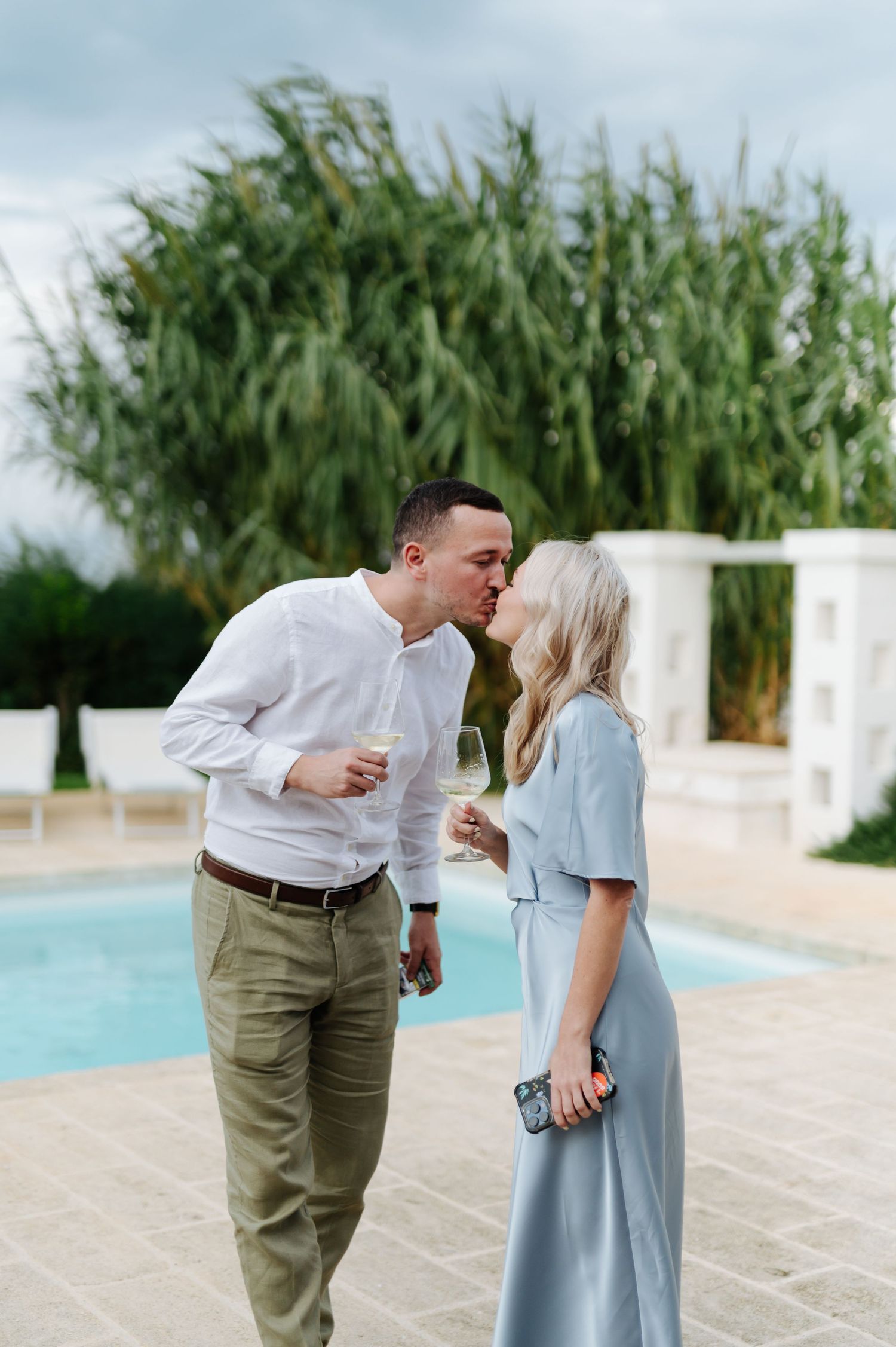 Couple sharing an intimate moment by a pool with lush greenery in background.