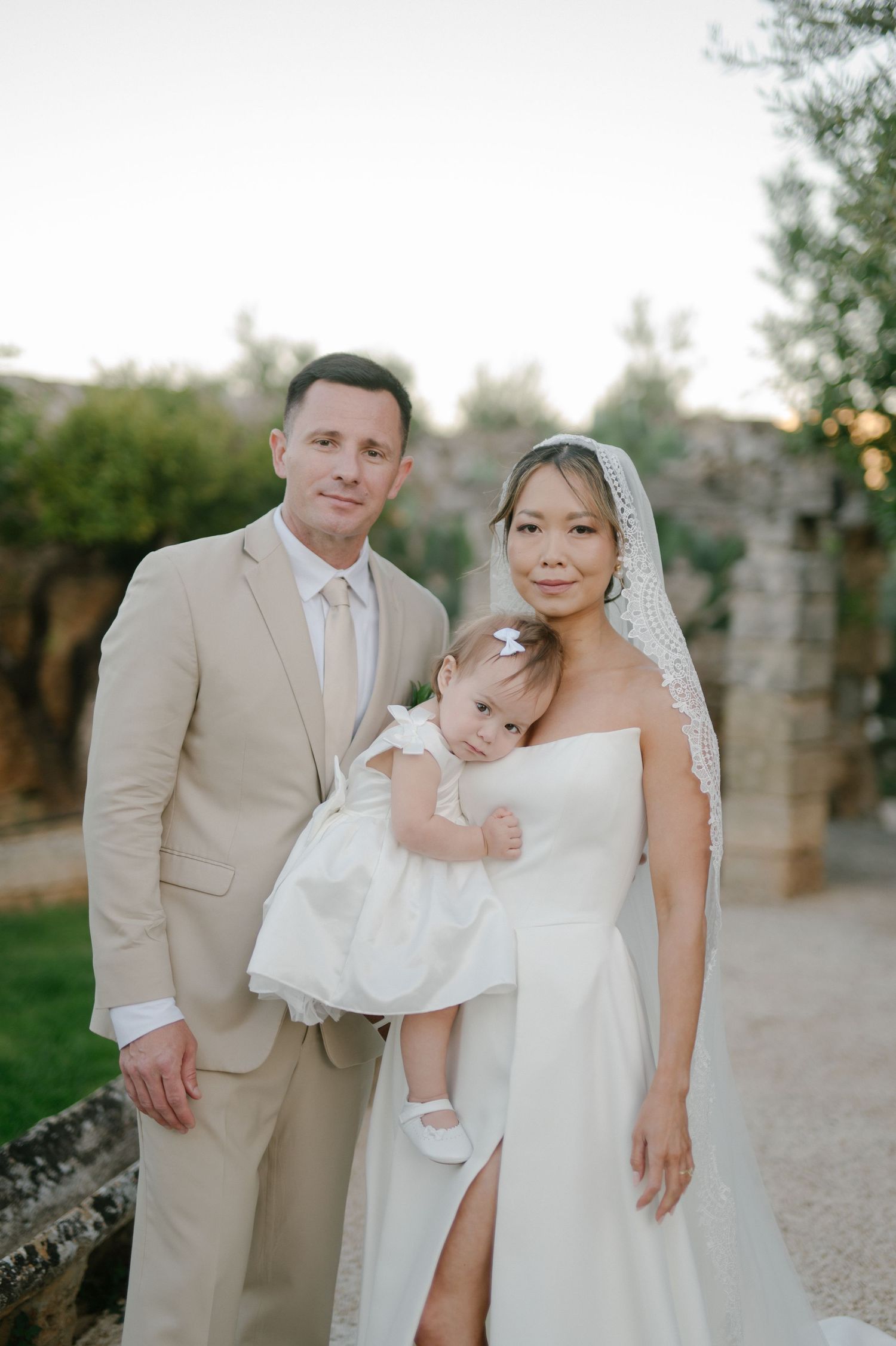 A romantic wedding couple poses together outdoors in a garden setting at sunset.