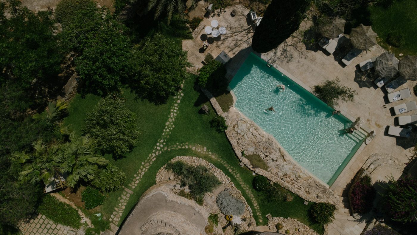 Aerial view of a luxury resort pool surrounded by lush landscaping and stone architecture.