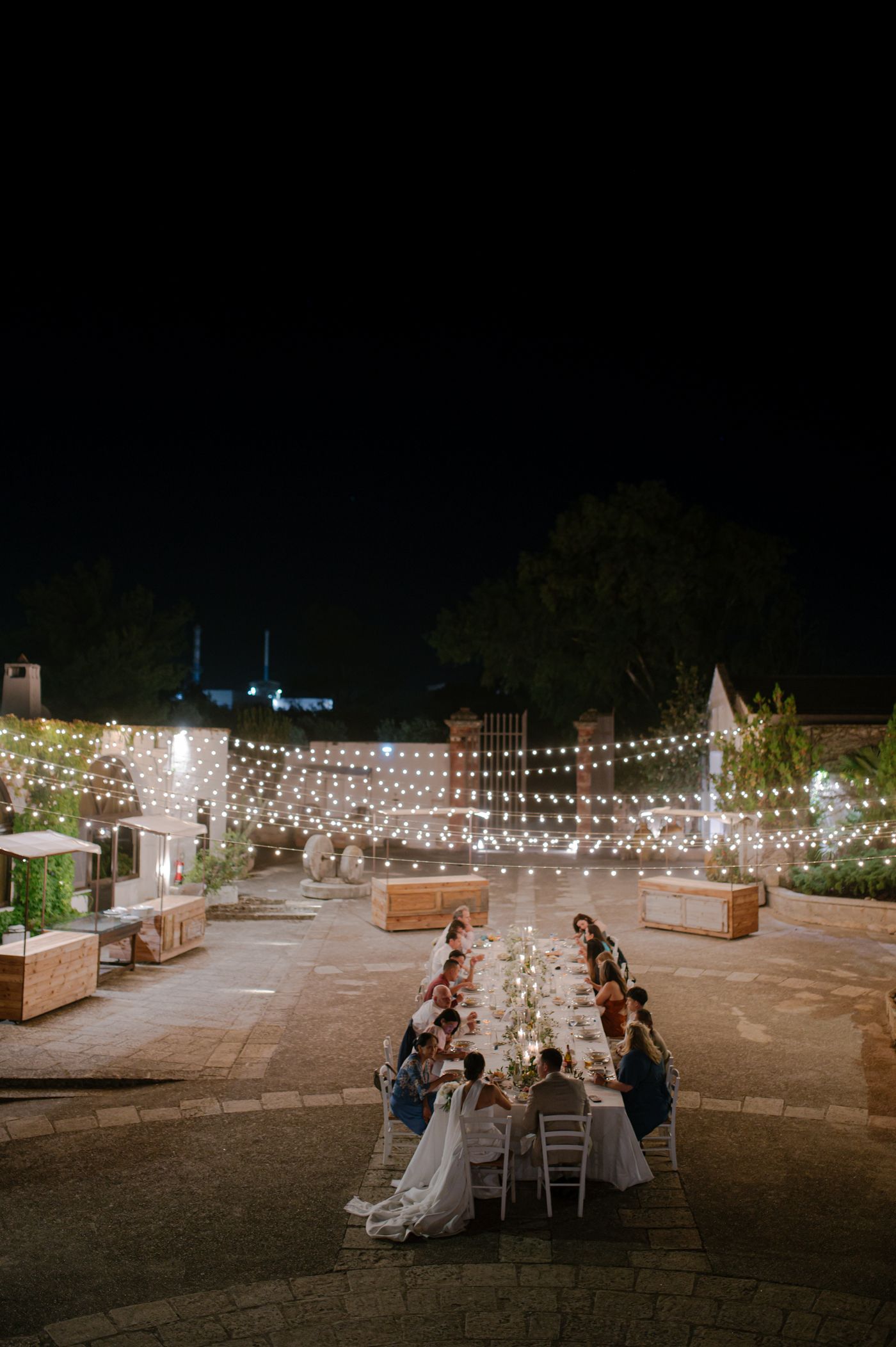 Outdoor wedding reception at night with string lights creating a magical ambiance across a stone patio area.