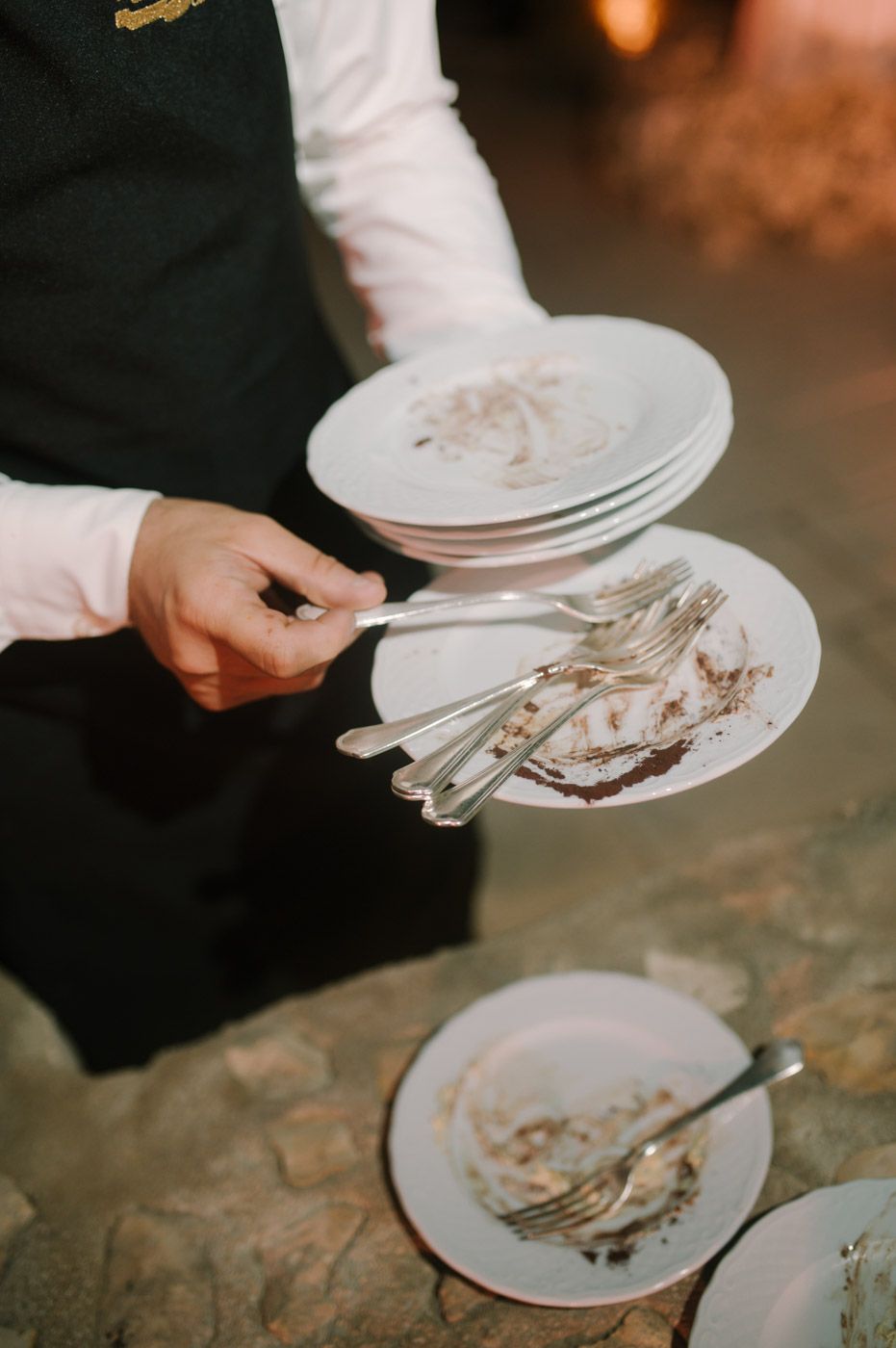 Server collecting used plates with cake remnants at a wedding reception.