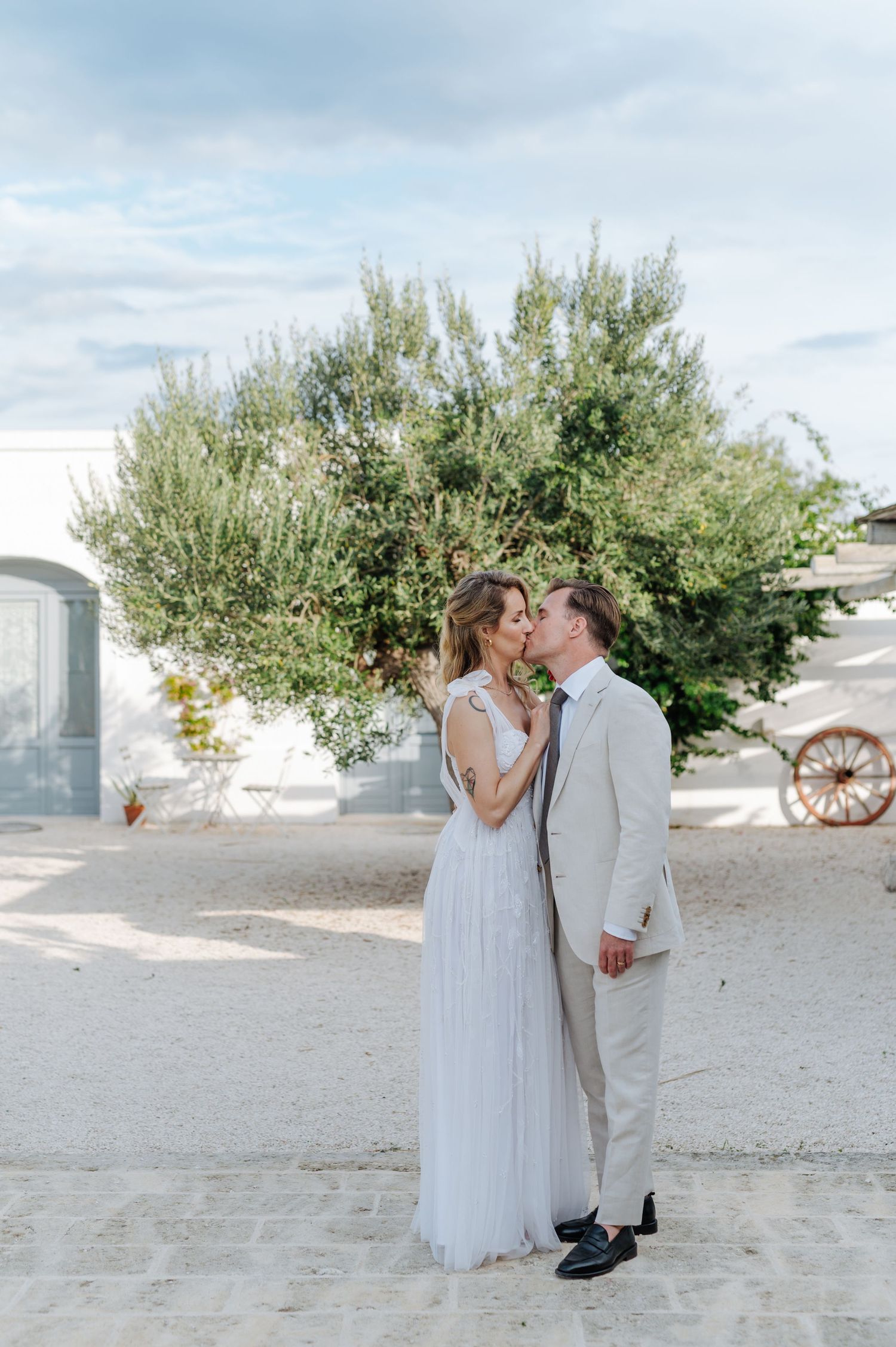Romantic moment between couple near olive trees and white buildings.