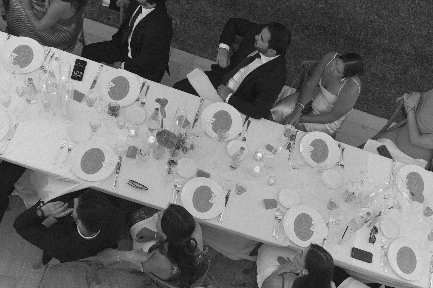 Aerial black and white view of wedding guests seated at a long elegantly set dining table.