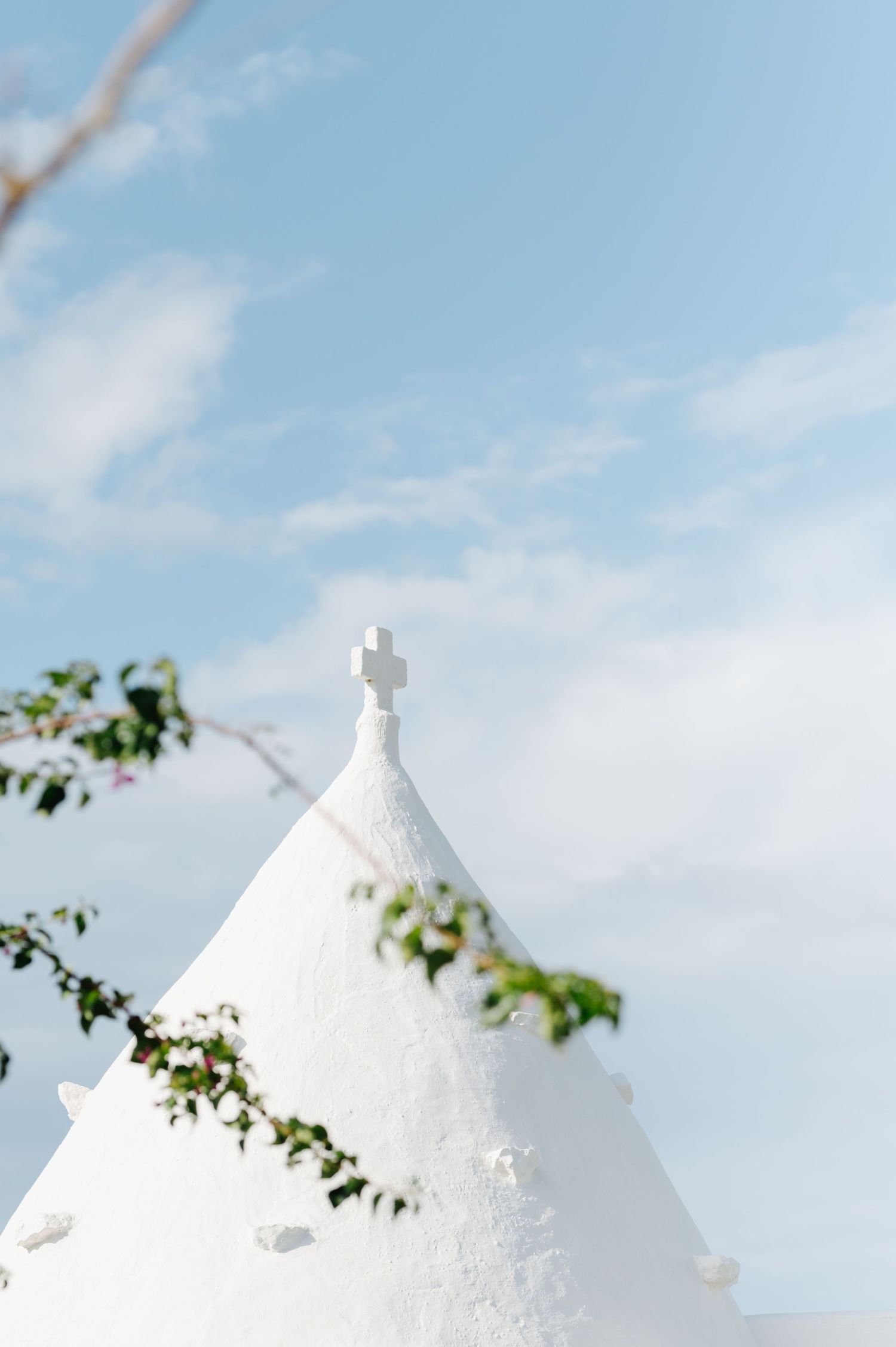 Traditional white trulli houses with conical roofs against bright blue sky.