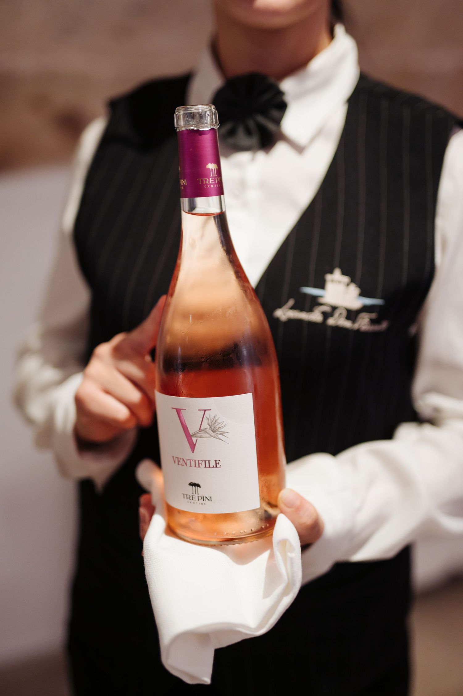 Server in formal attire presenting bottles of rose wine at an elegant event.