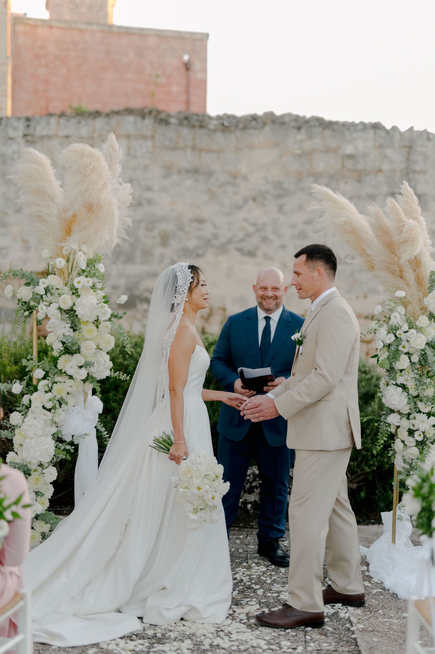 Outdoor wedding ceremony with white floral arrangements and brick backdrop.