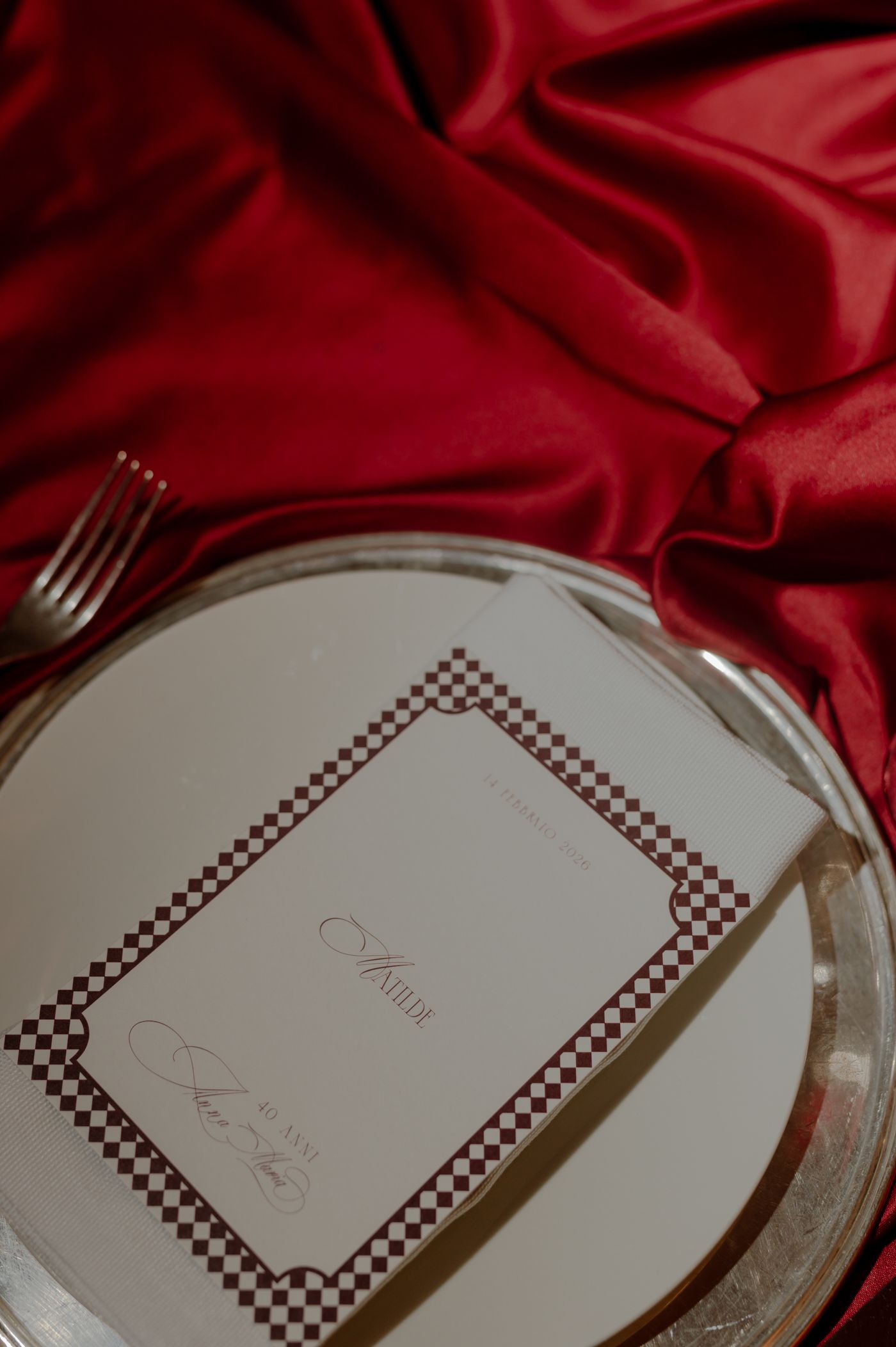 Elegant white plates with decorative brown checkered borders arranged on a luxurious red satin tablecloth.