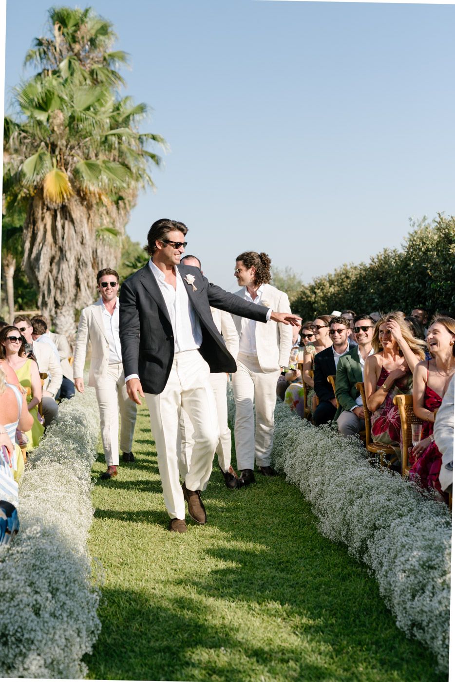 Outdoor wedding celebration with white floral arrangements and palm trees.