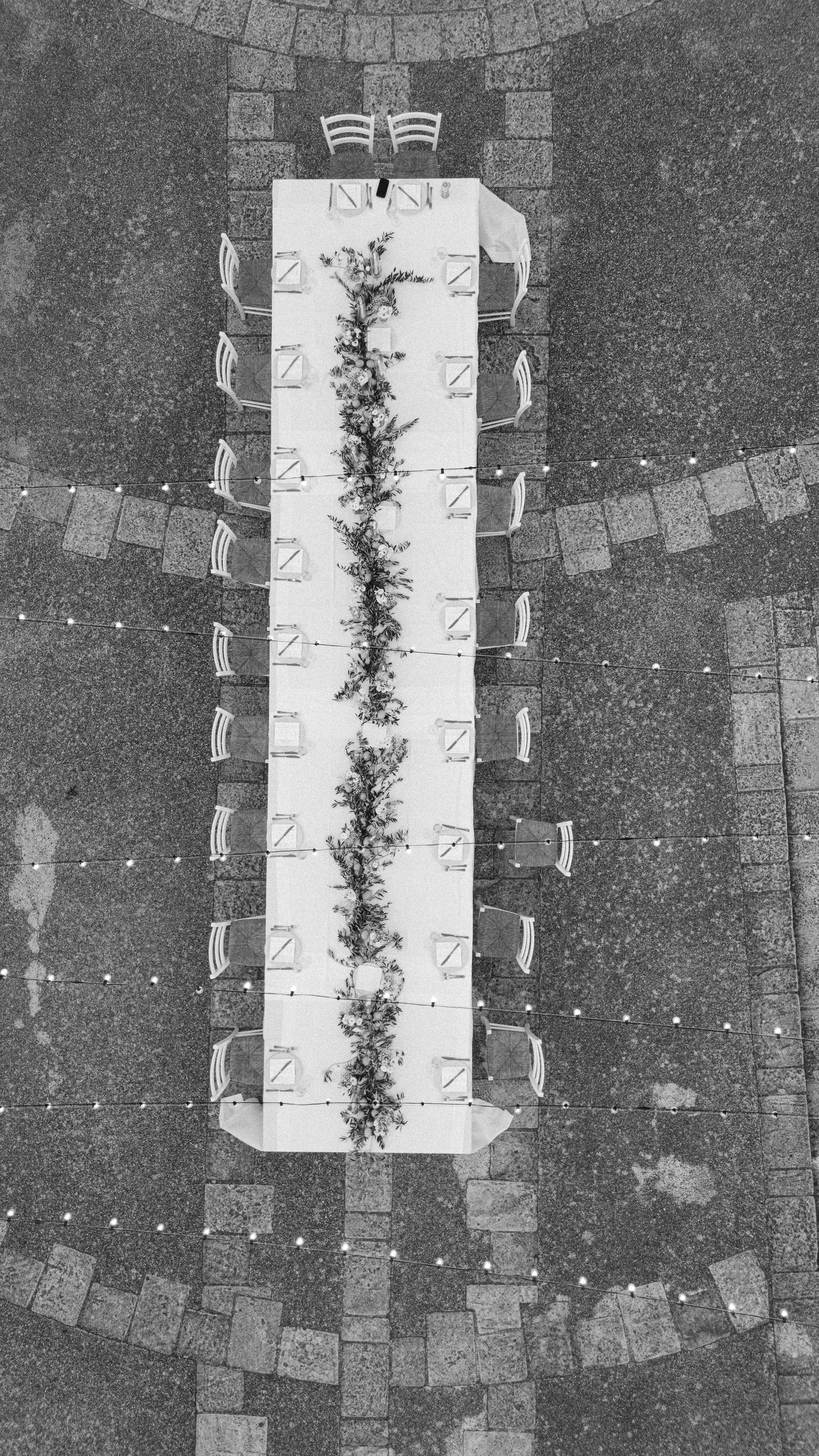 Aerial view of long white banquet tables with floral centerpieces and chairs arranged in a dark space.