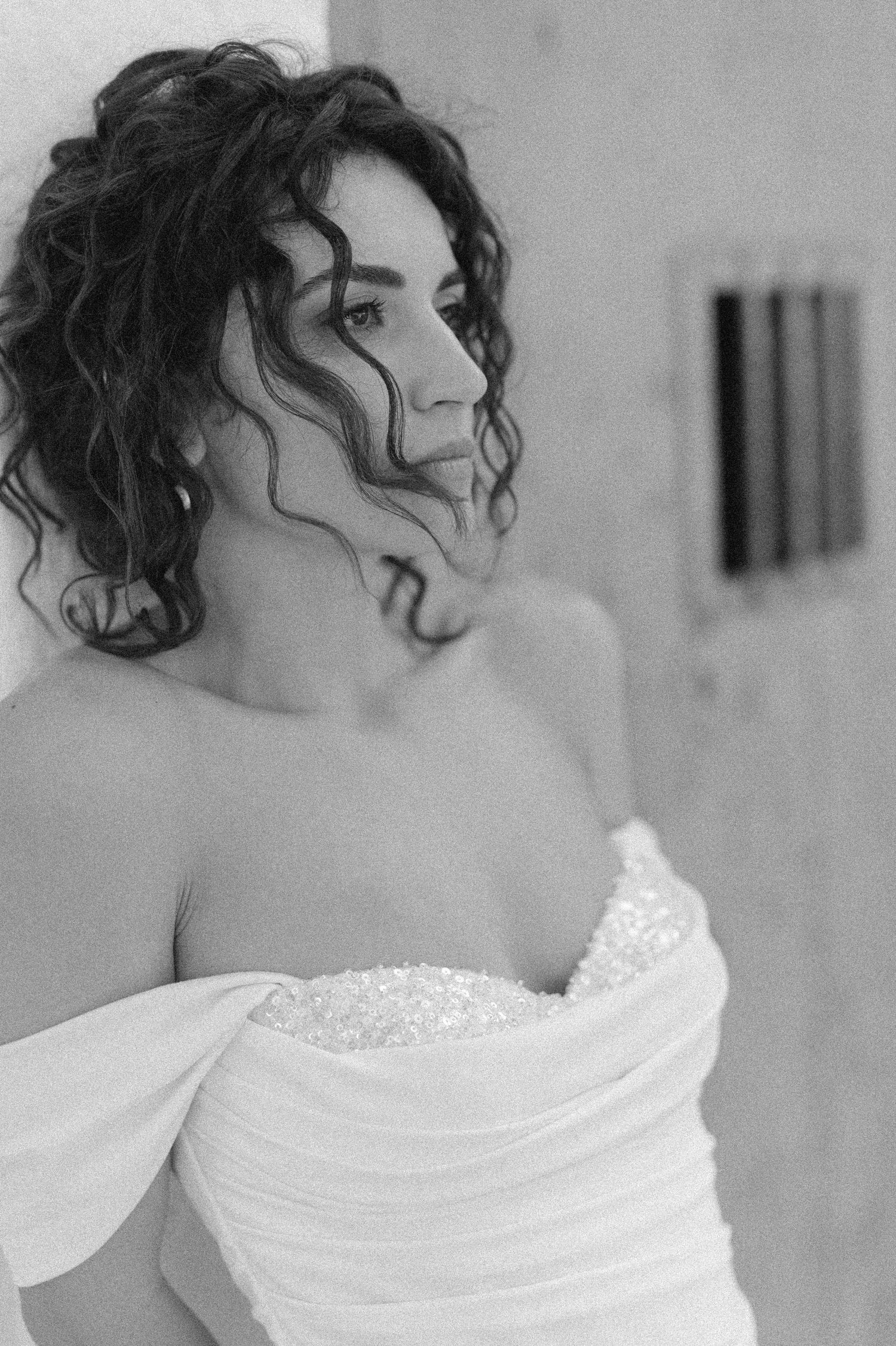 Black and white portrait of a bride in an off-shoulder wedding dress with curly hair.