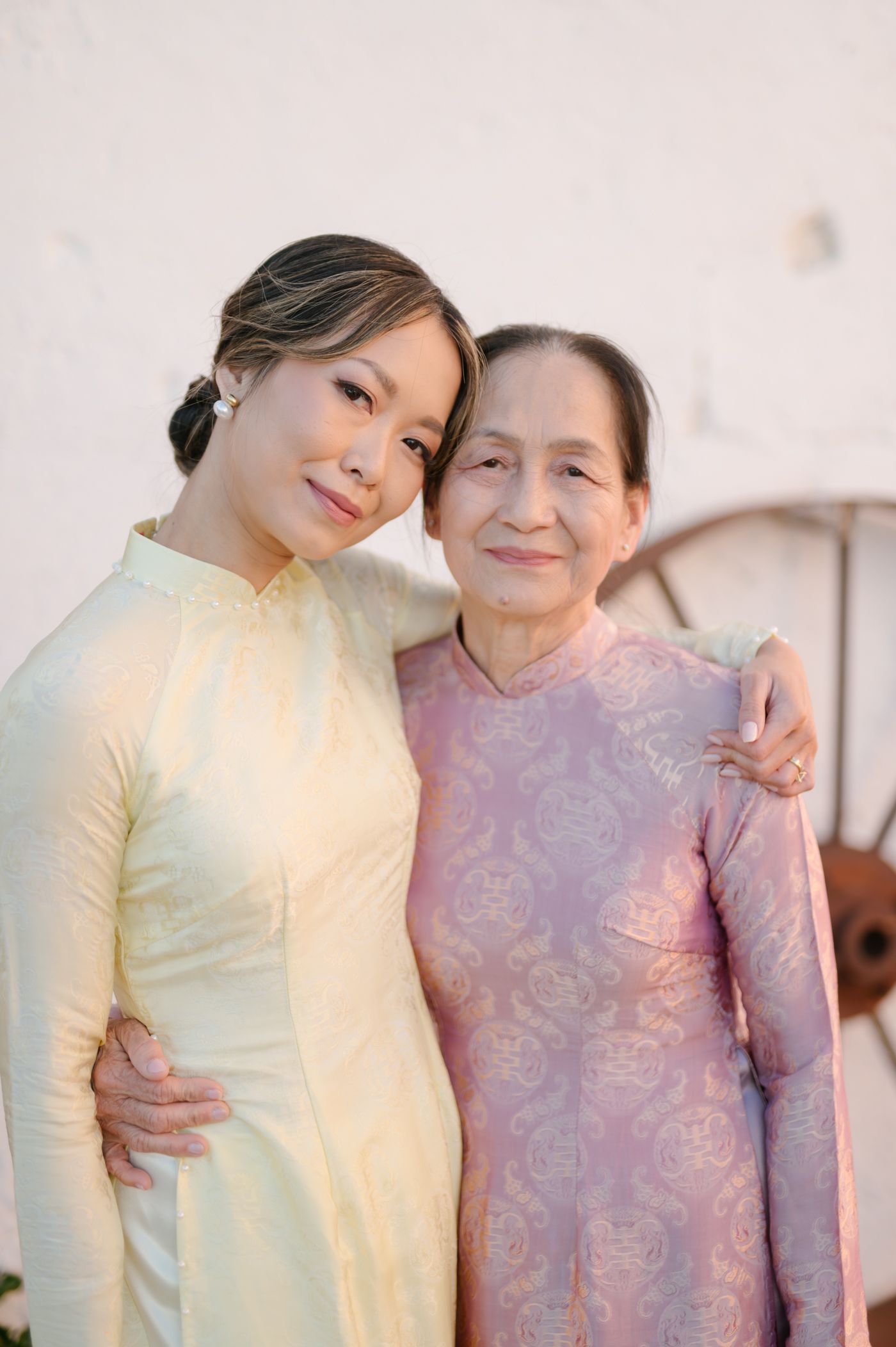 Two women in traditional Vietnamese ao dai dresses embrace warmly while posing together for a portrait series.