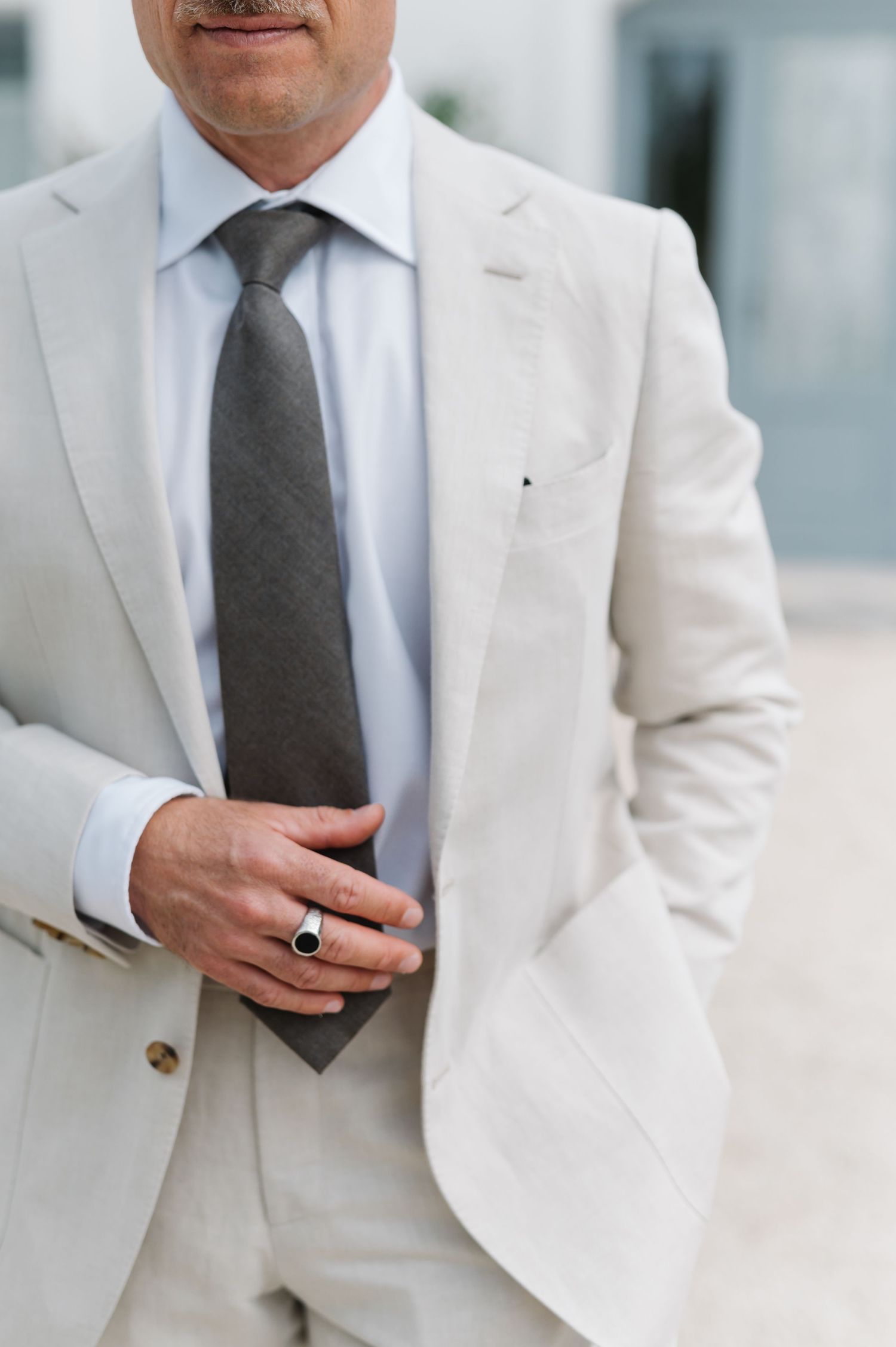 Close-up details of a light colored suit with gray tie against white architecture.
