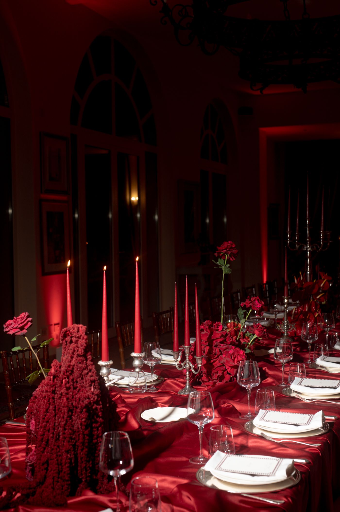 Elegant table settings with white plates and red decor in dramatic lighting create a romantic dining atmosphere.