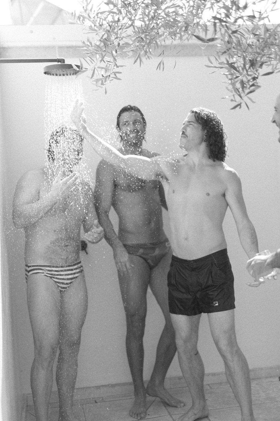 Group of people in swimwear standing against a white wall outdoors.