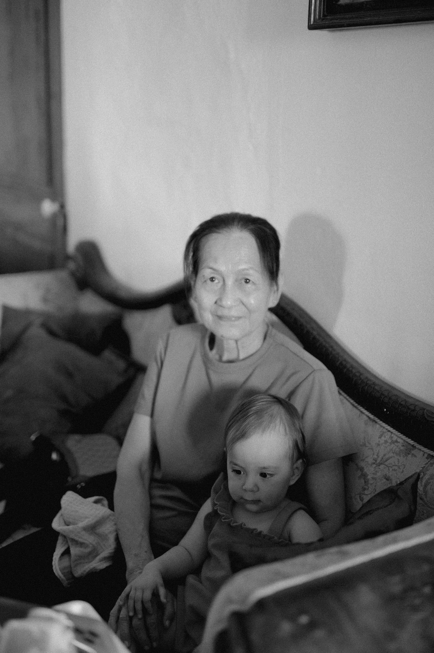 A black and white photograph shows an elderly person sitting on a couch with a small child in a casual home setting.