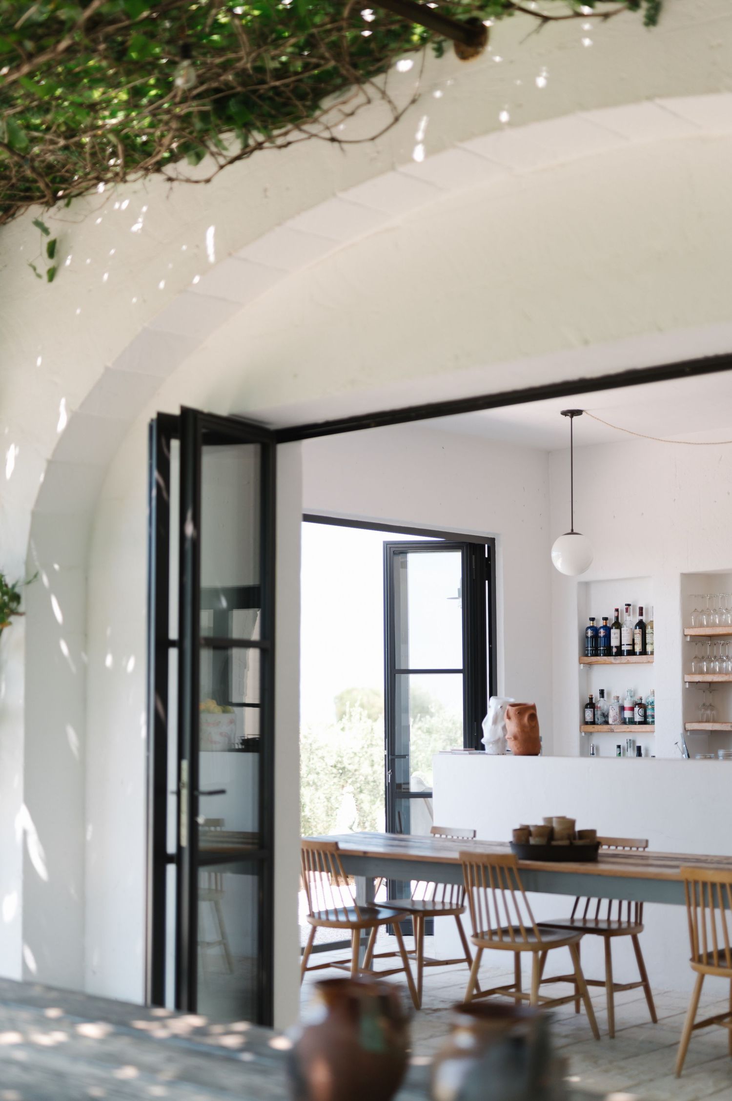 Modern white dining room with wooden chairs and black-framed glass doors showcases minimalist Scandinavian design elements.