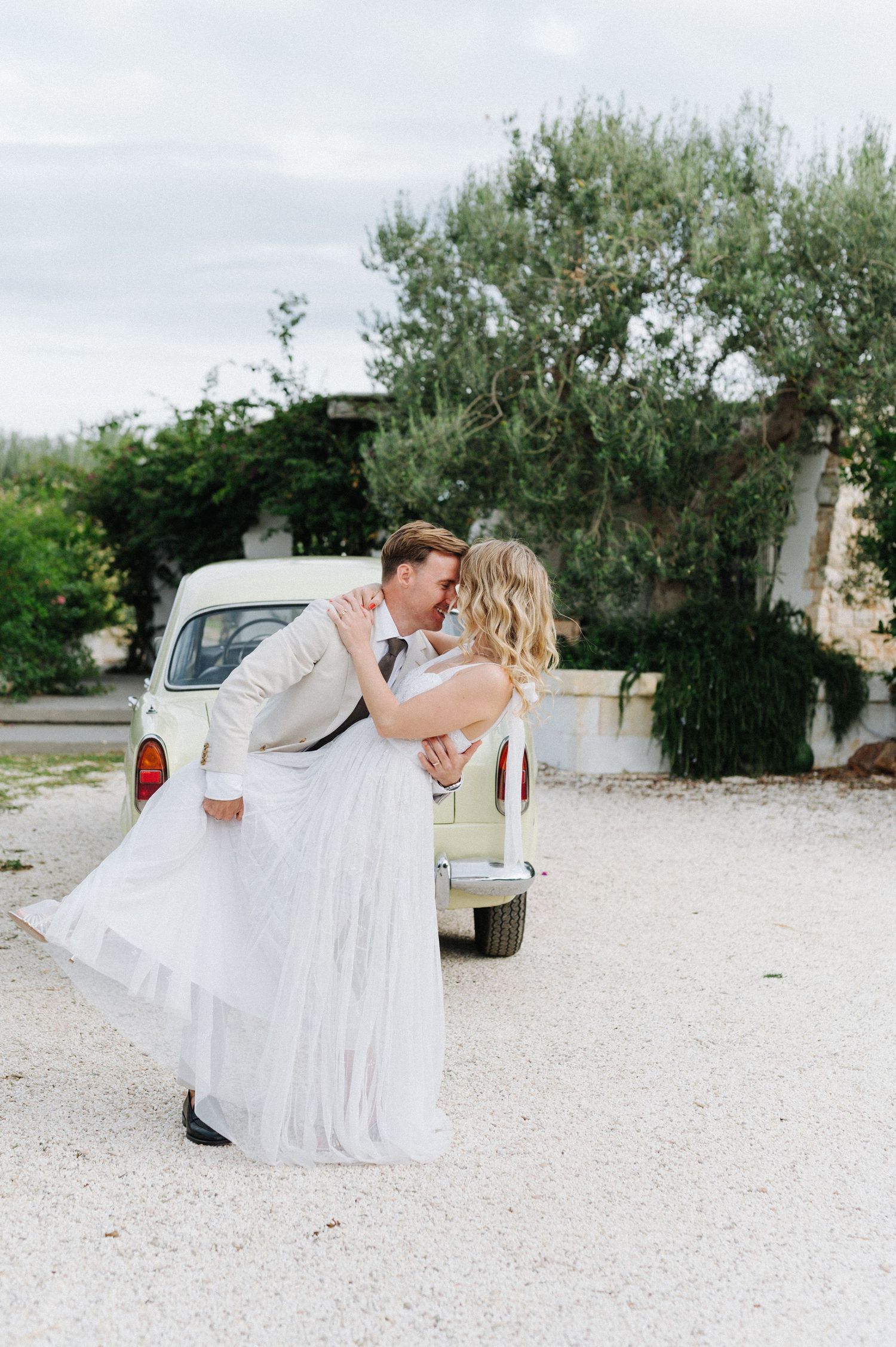 Romantic wedding couple embracing near a vintage car on their special day.