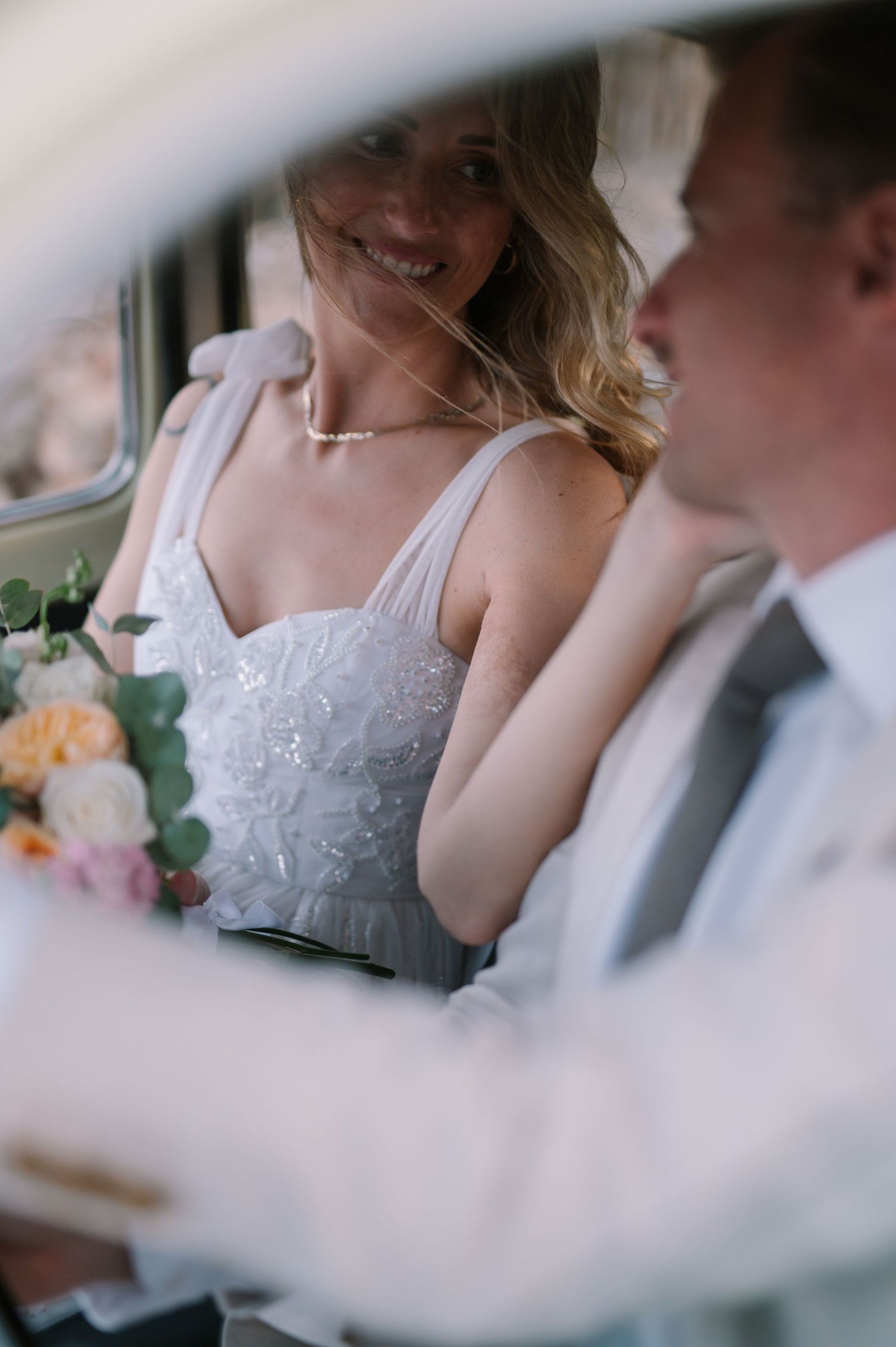 Wedding couple sitting close together in formal attire inside a vehicle.