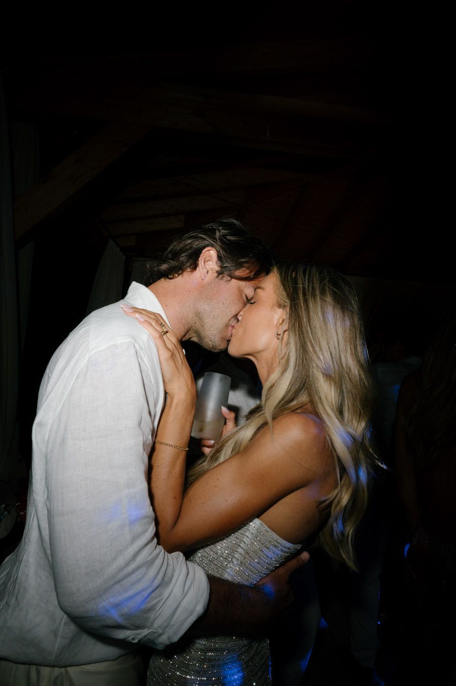 A couple shares a romantic kiss in a dimly lit room with blue lighting in the background.