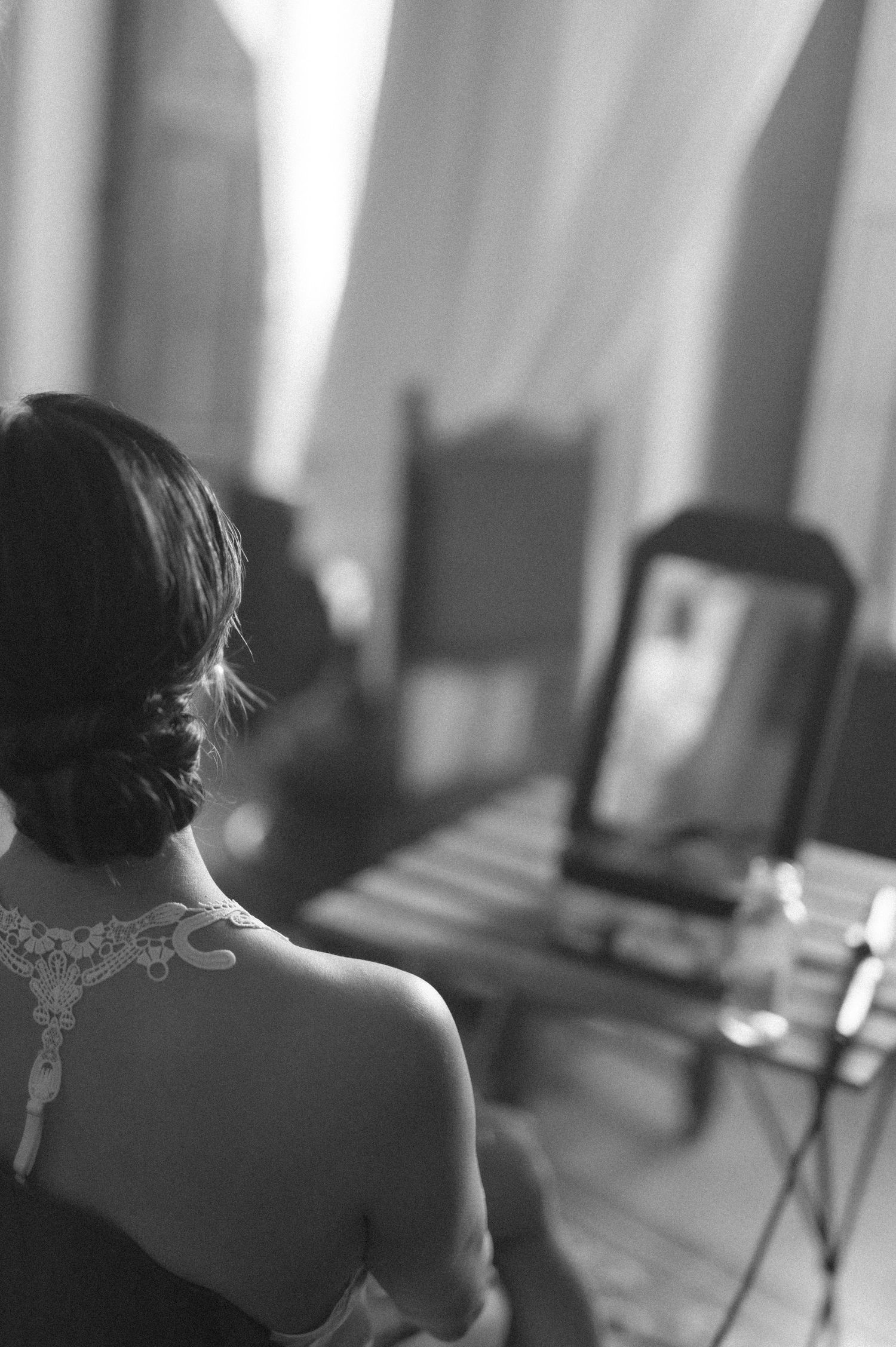 A person in a lace-back dress sits in front of a tablet or device for a video call in black and white photography.