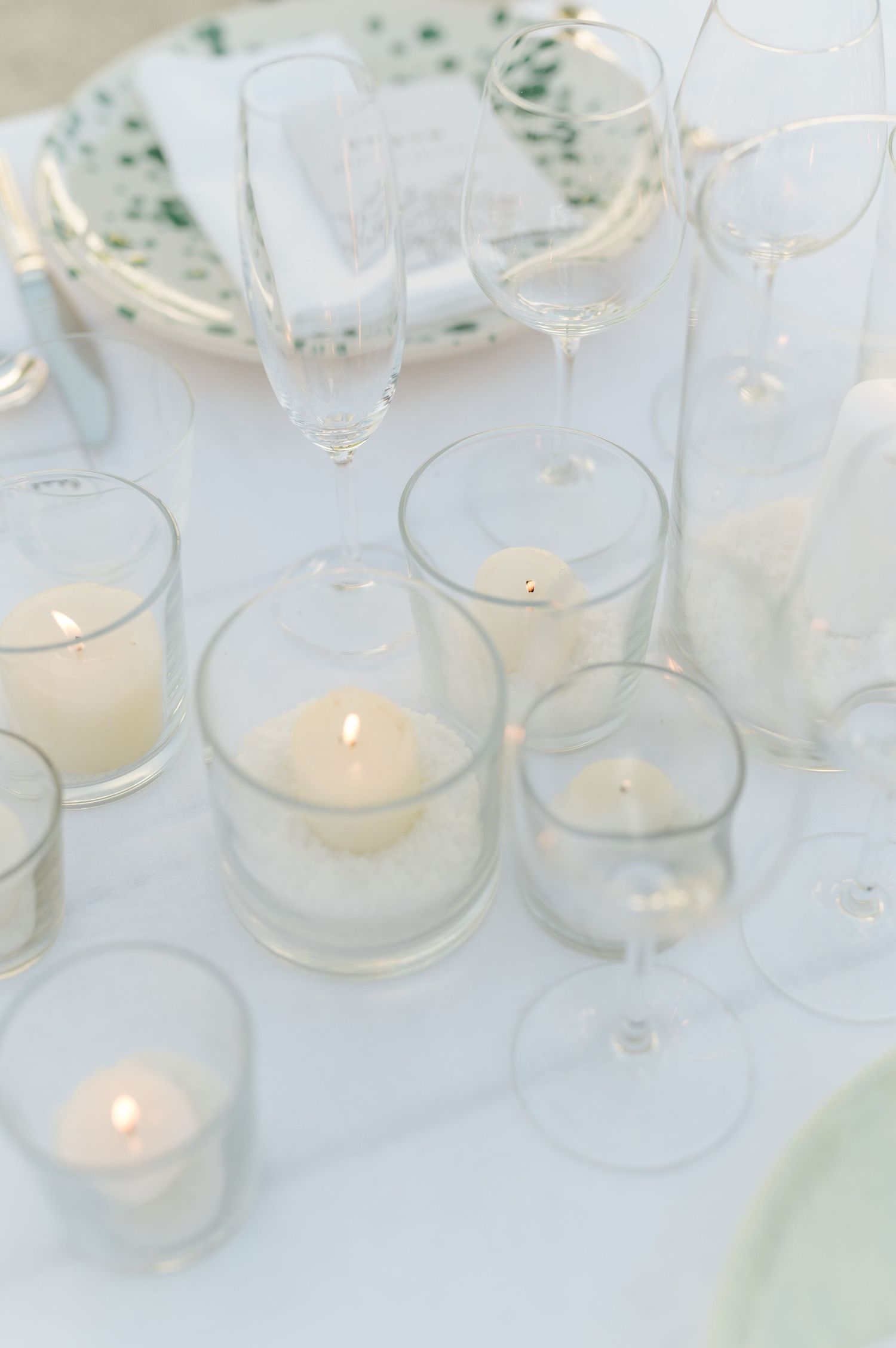 White tea light candles in glass holders create a soft, romantic glow on a white tablecloth.