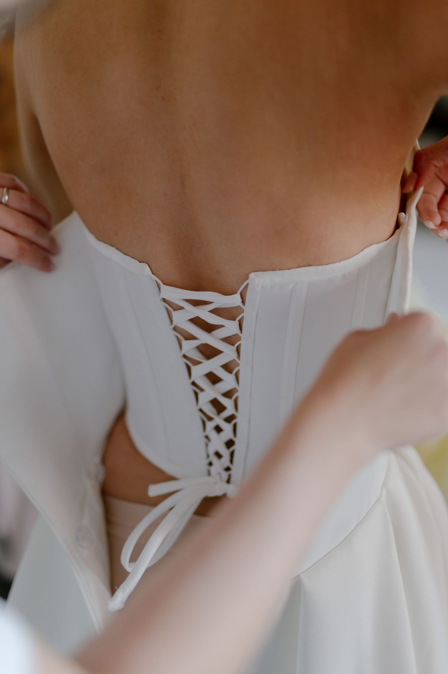 Close-up view of a white corset-style dress being laced up with satin ribbon through decorative eyelets.