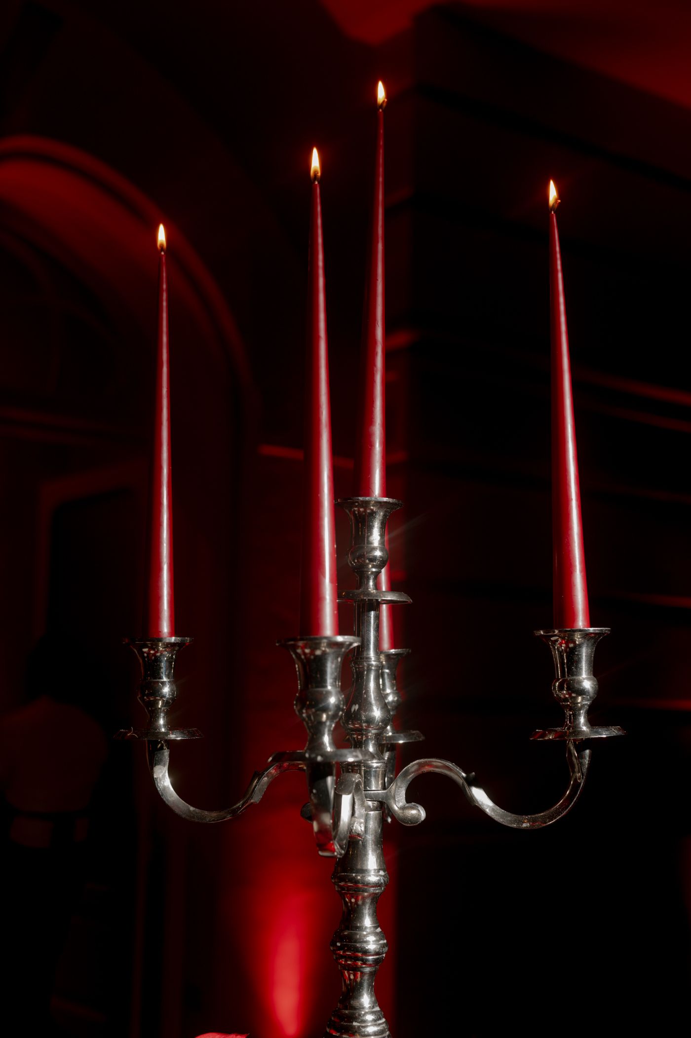 Silver candelabra with four lit red candles glowing against a dark red background.