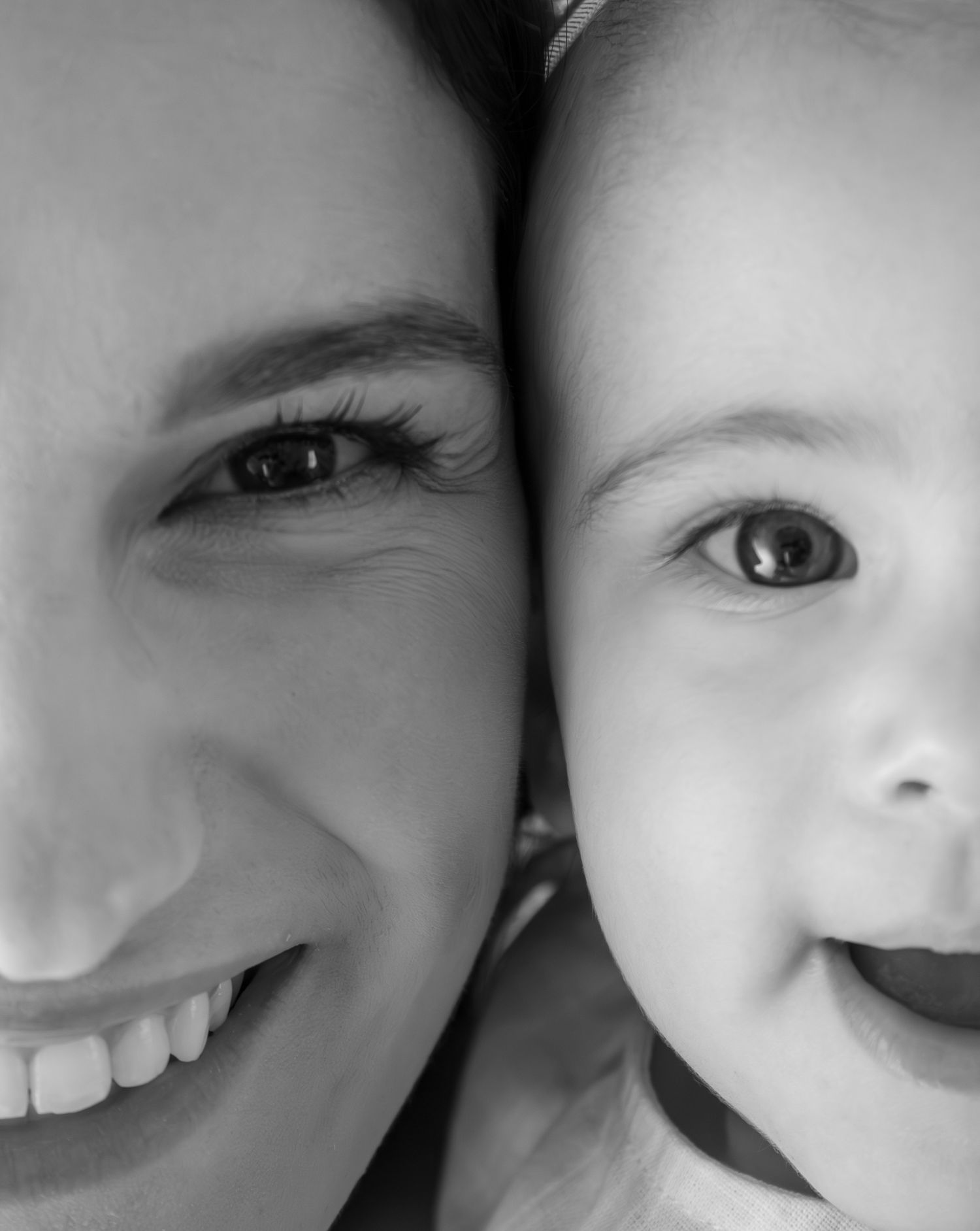 Black and white close-up portrait of a smiling mother and happy baby cheek to cheek.