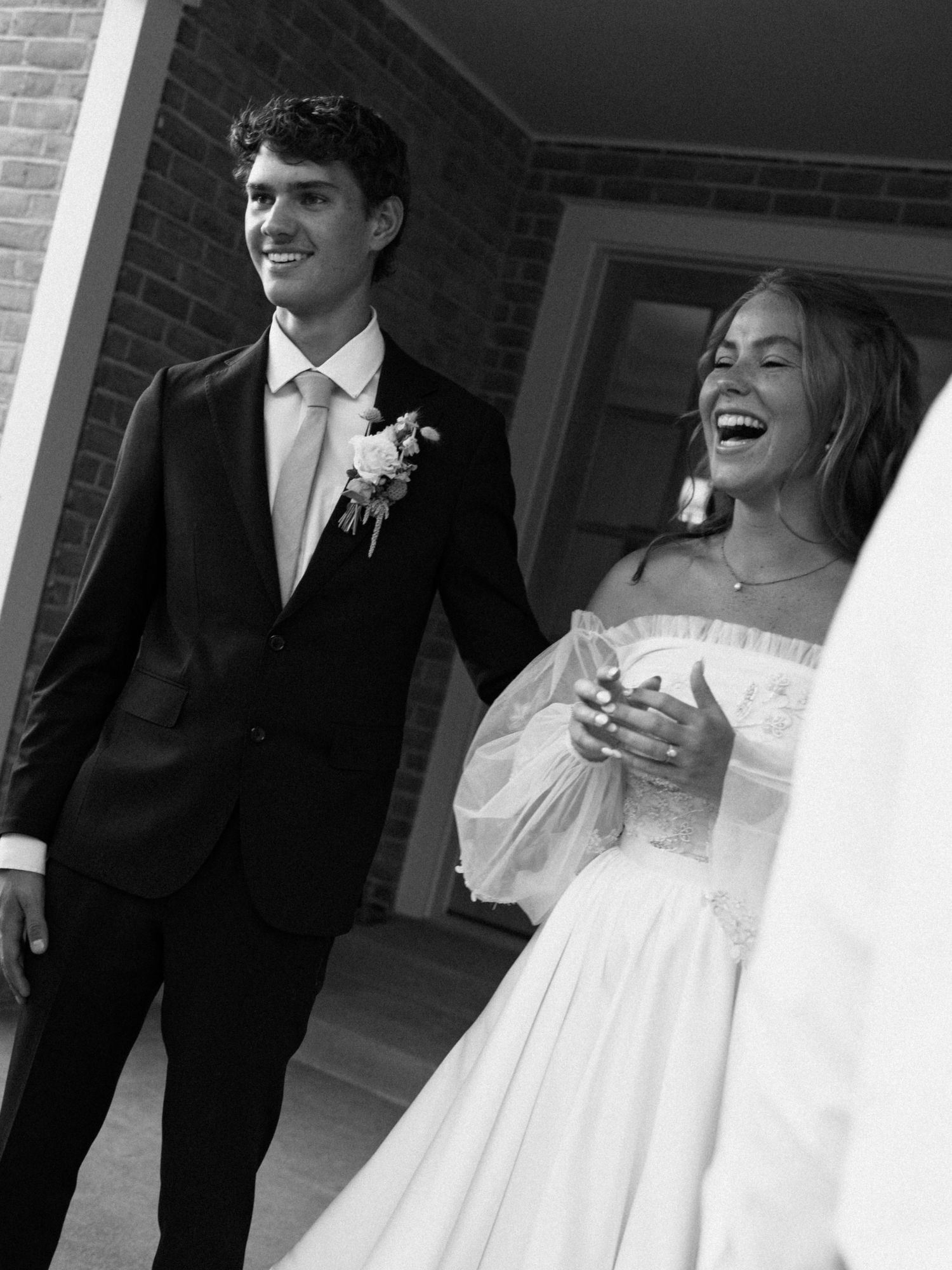 A black and white wedding photograph showing a candid moment between a couple on a porch with white columns.