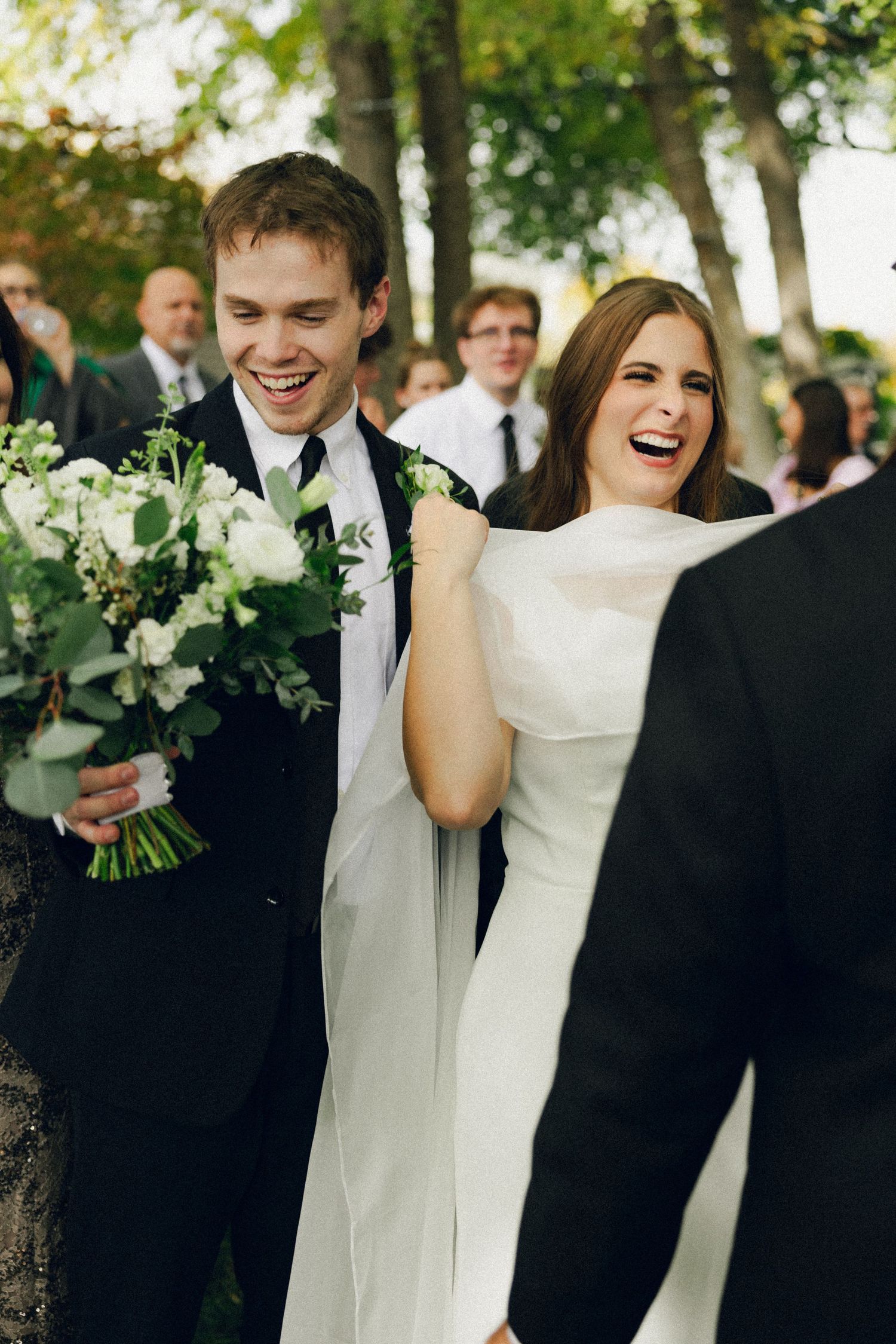 A joyful wedding moment captured in black and white showing the happy couple laughing together outdoors.