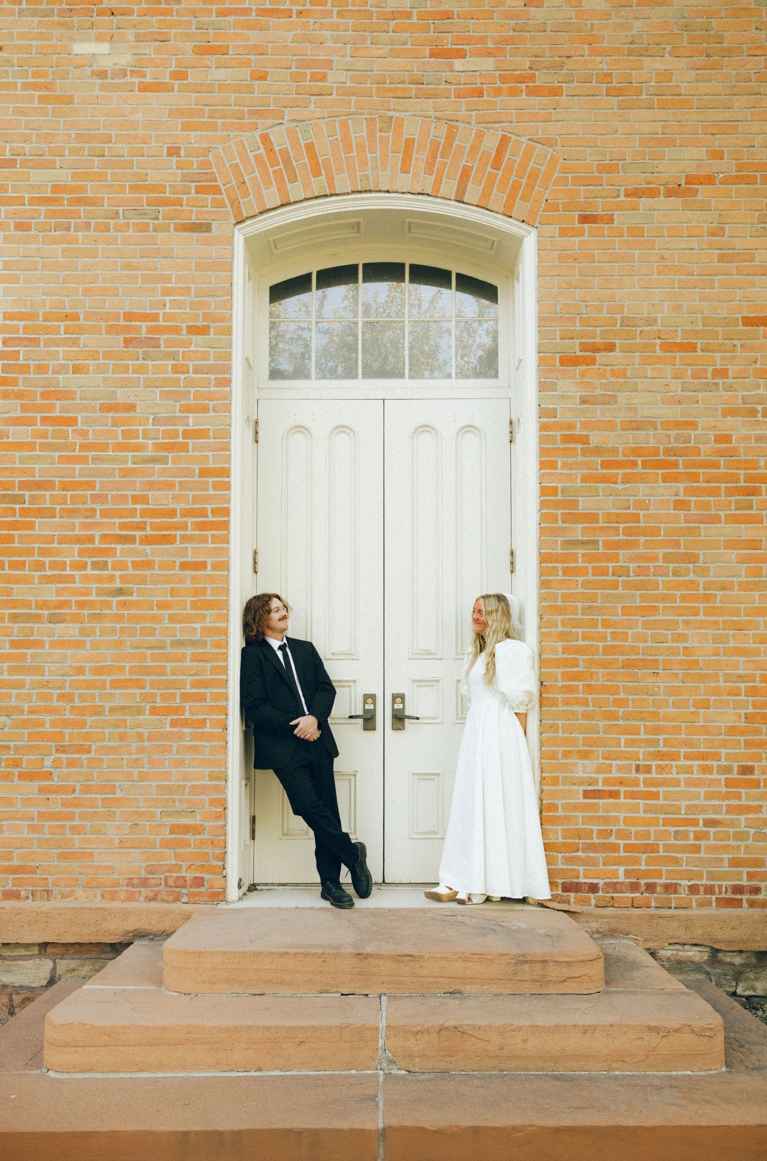 A series of four sequential photos showing two people interacting playfully on a brick building's doorstep.