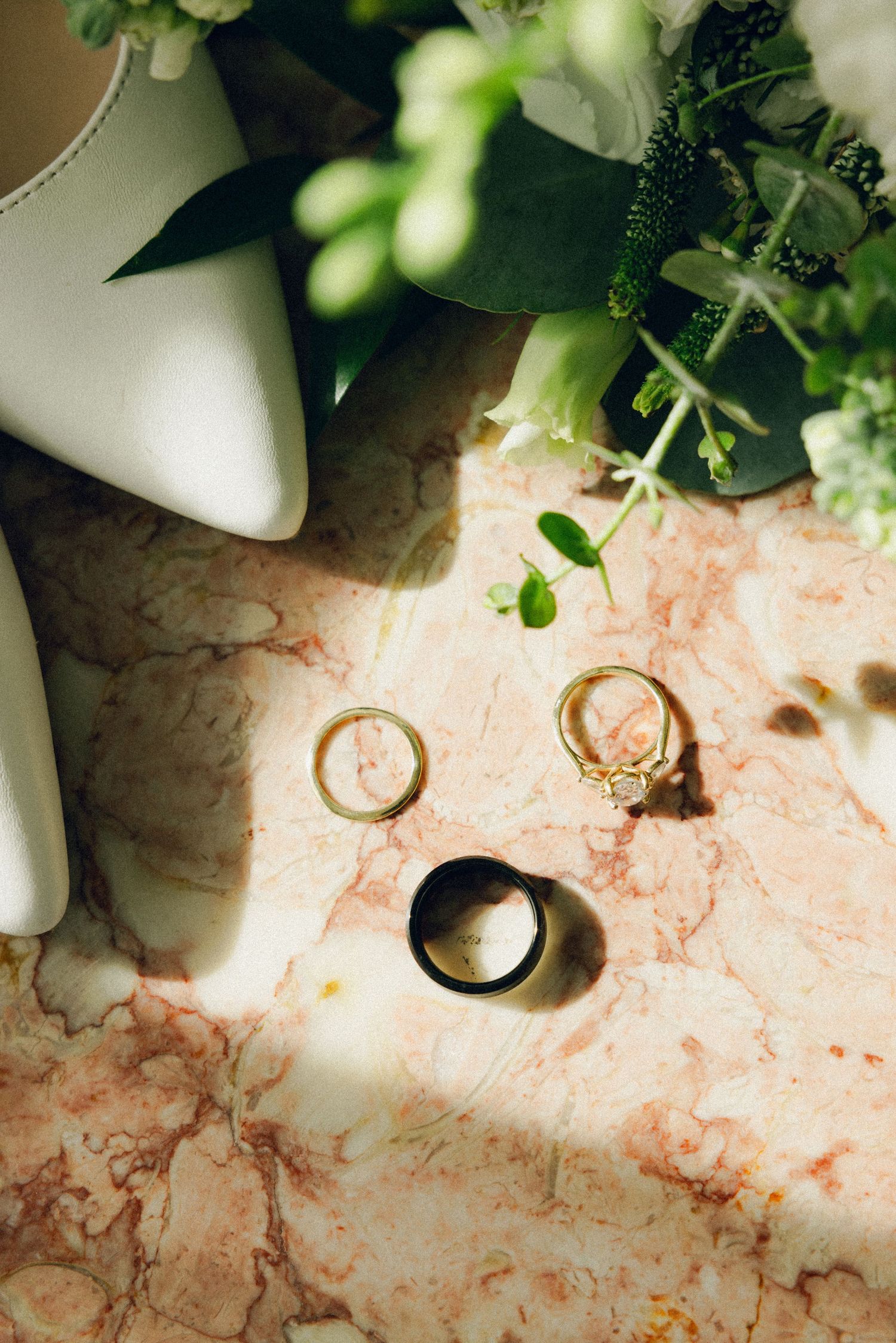 Wedding rings and delicate white flowers arranged on pink marble surface in elegant bridal detail shot.
