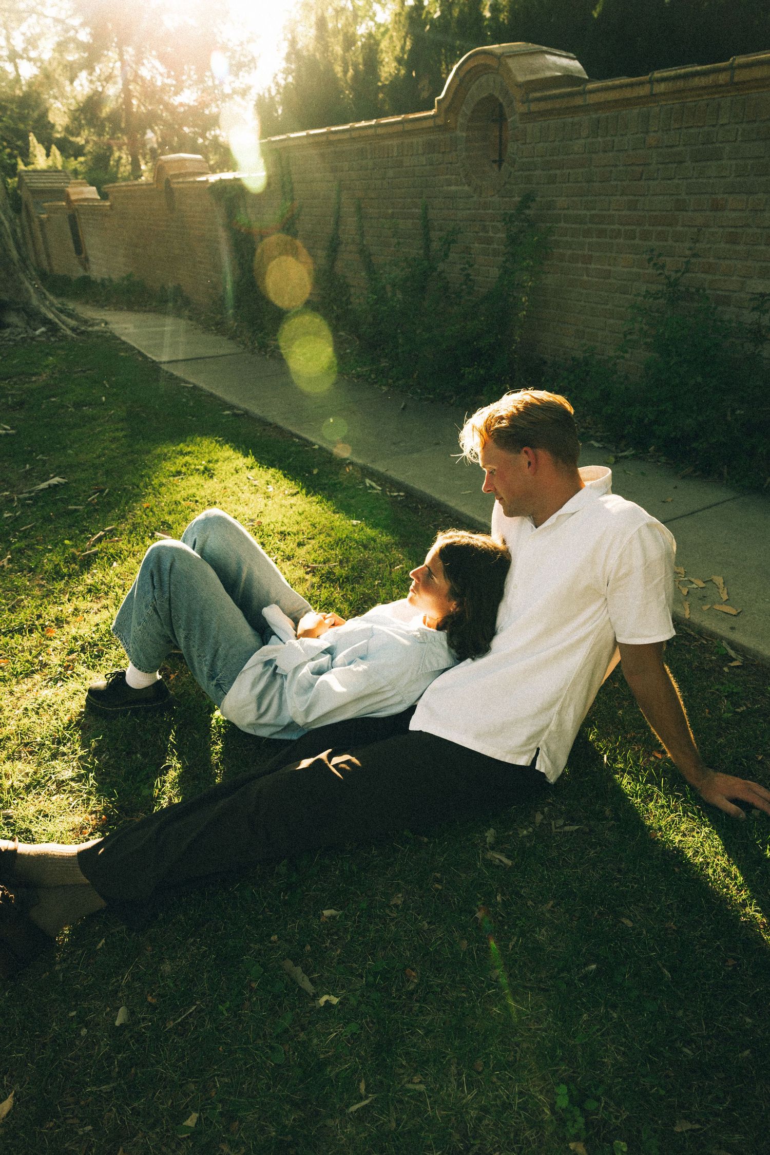 Two people lying on grass in warm sunlight with lens flare creating a dreamy atmosphere.