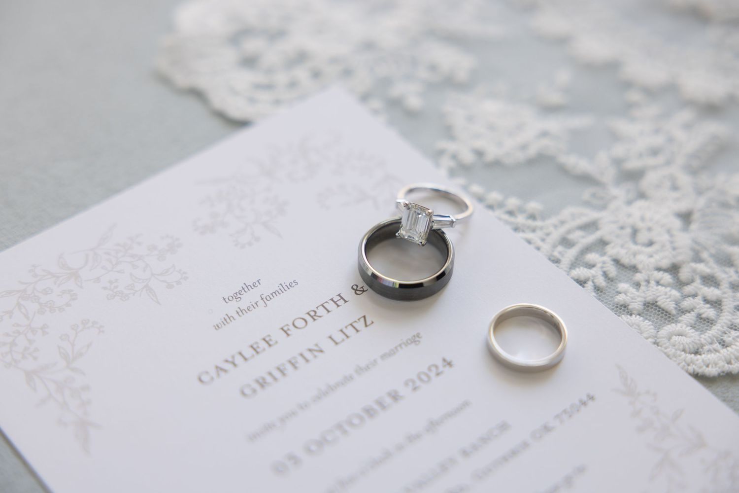 Wedding rings and invitation details on delicate white lace background.