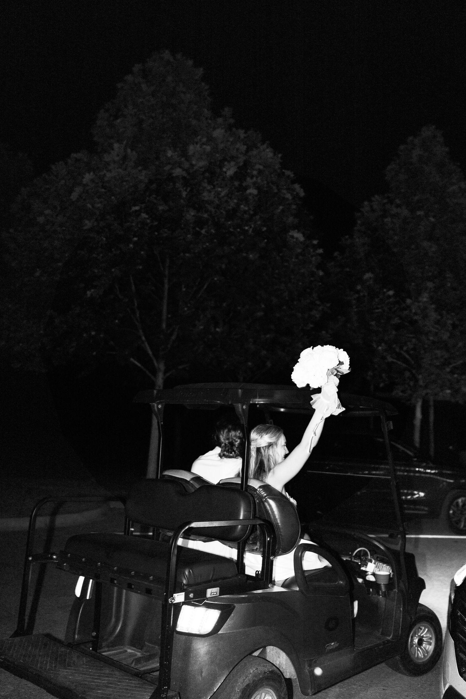 Newlyweds waving from a vintage car during their nighttime wedding departure.