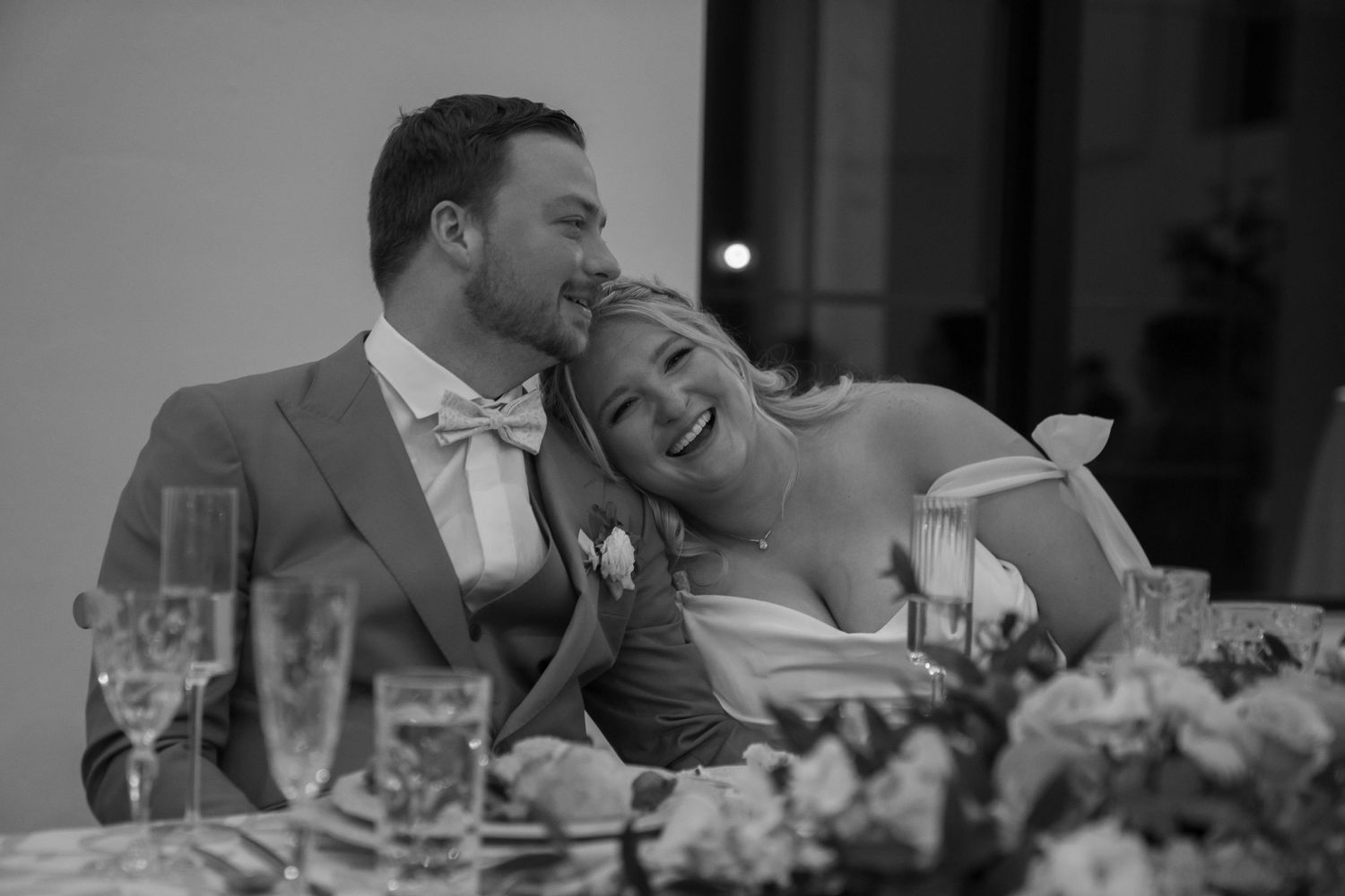 Wedding reception guests laughing and enjoying dinner at elegantly decorated tables.