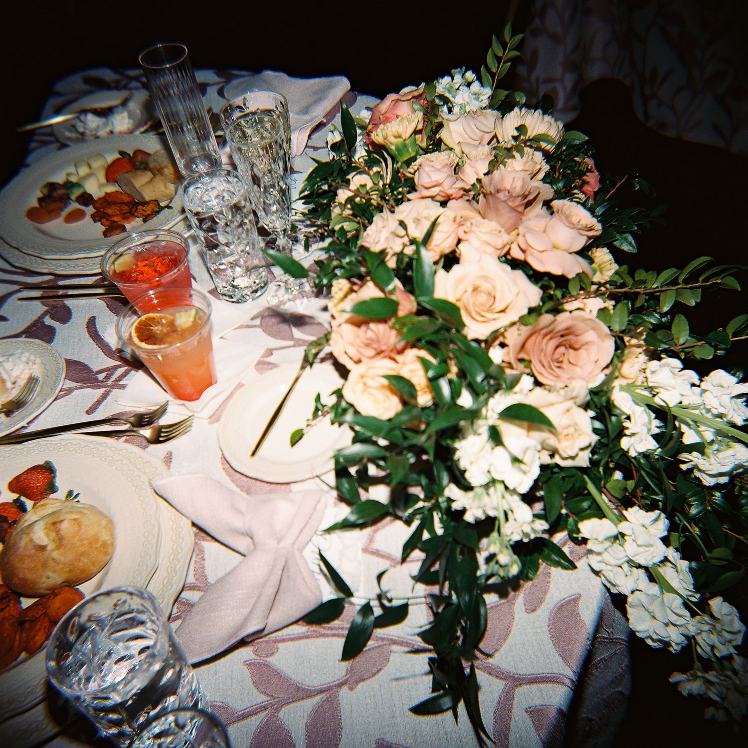 Elegant wedding reception table settings with pink and white floral centerpieces and crystal glassware in soft lighting.