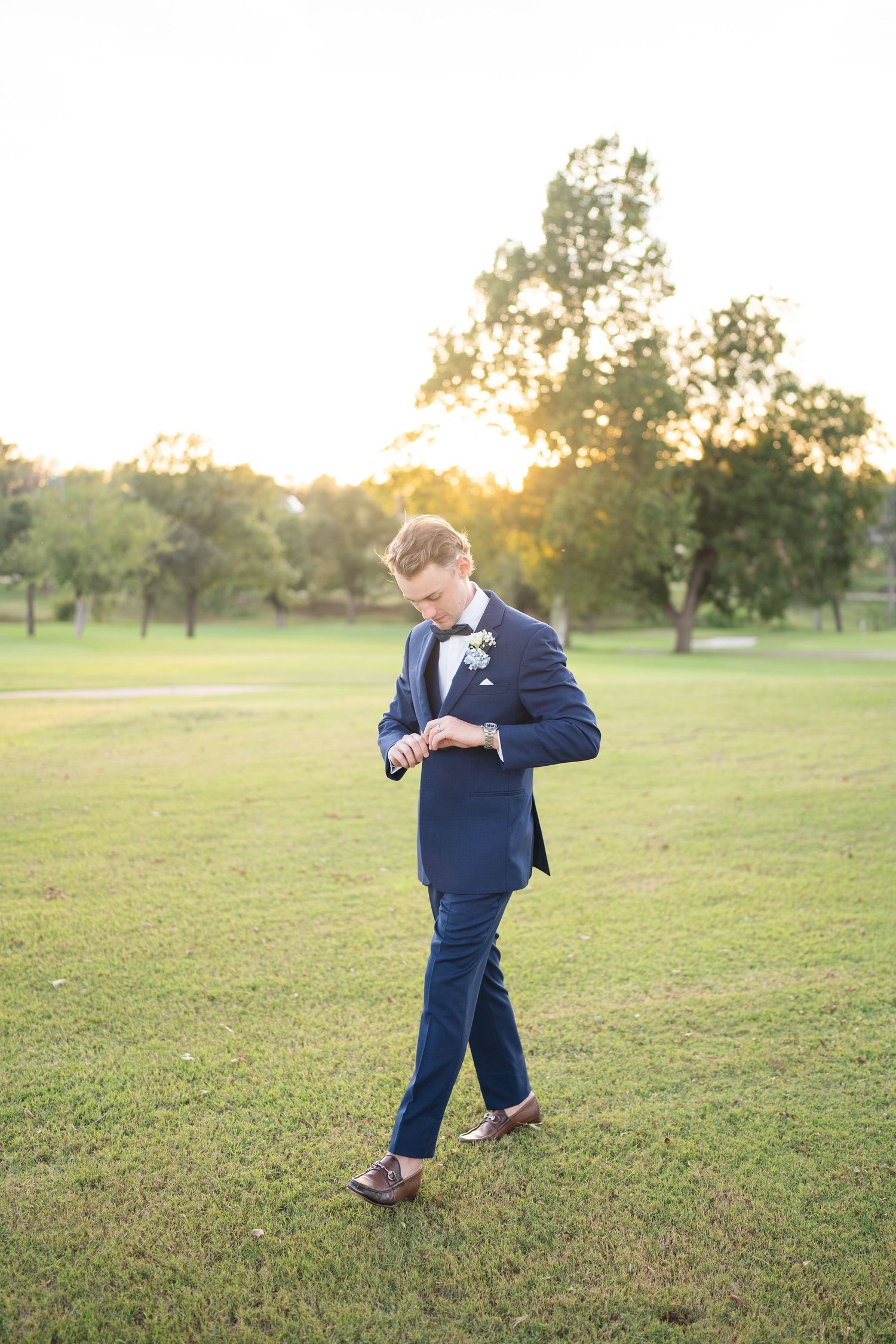 Young ring bearer in navy suit plays on grassy field during wedding.