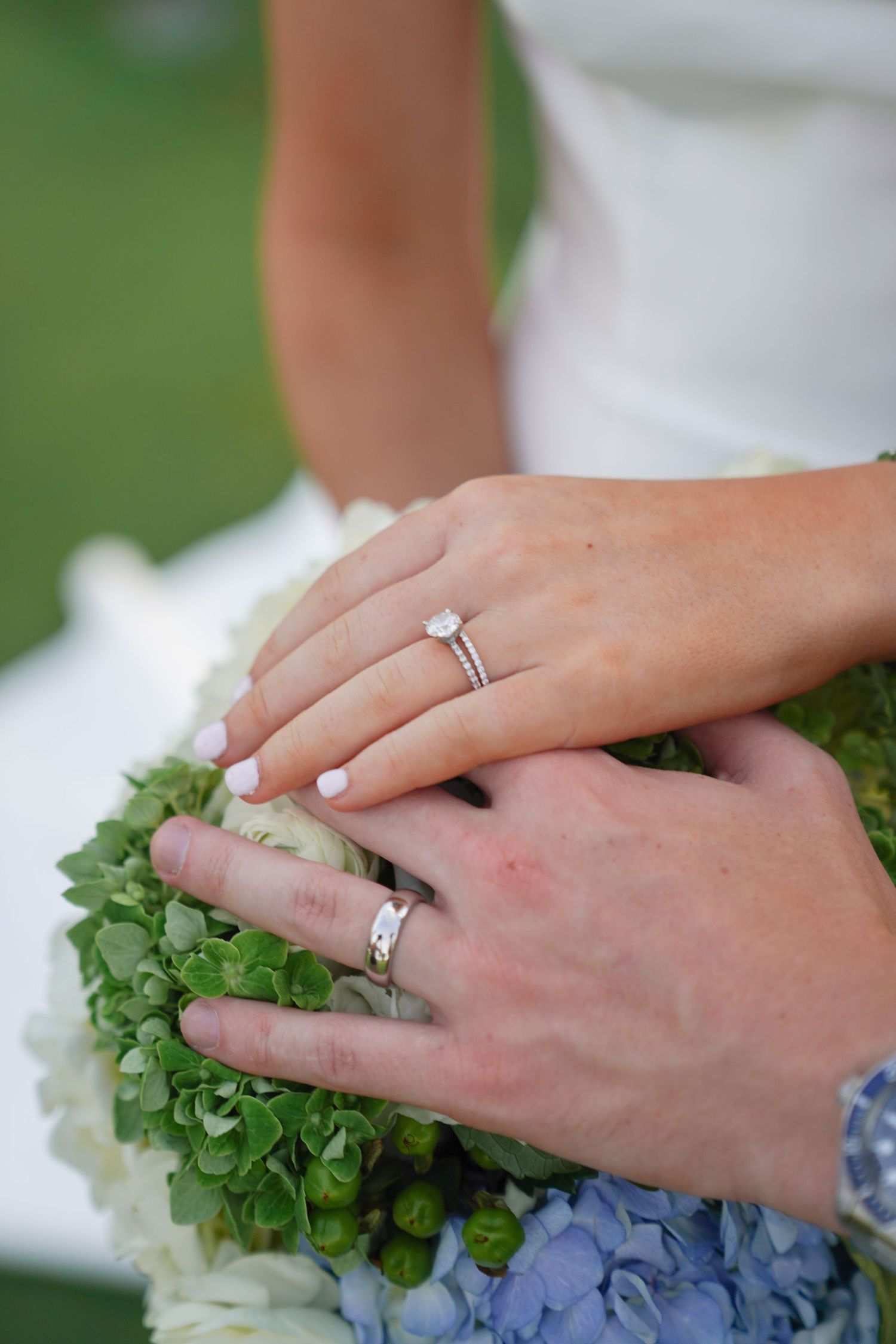Close-up of wedding rings and hands holding a hydrangea bouquet.