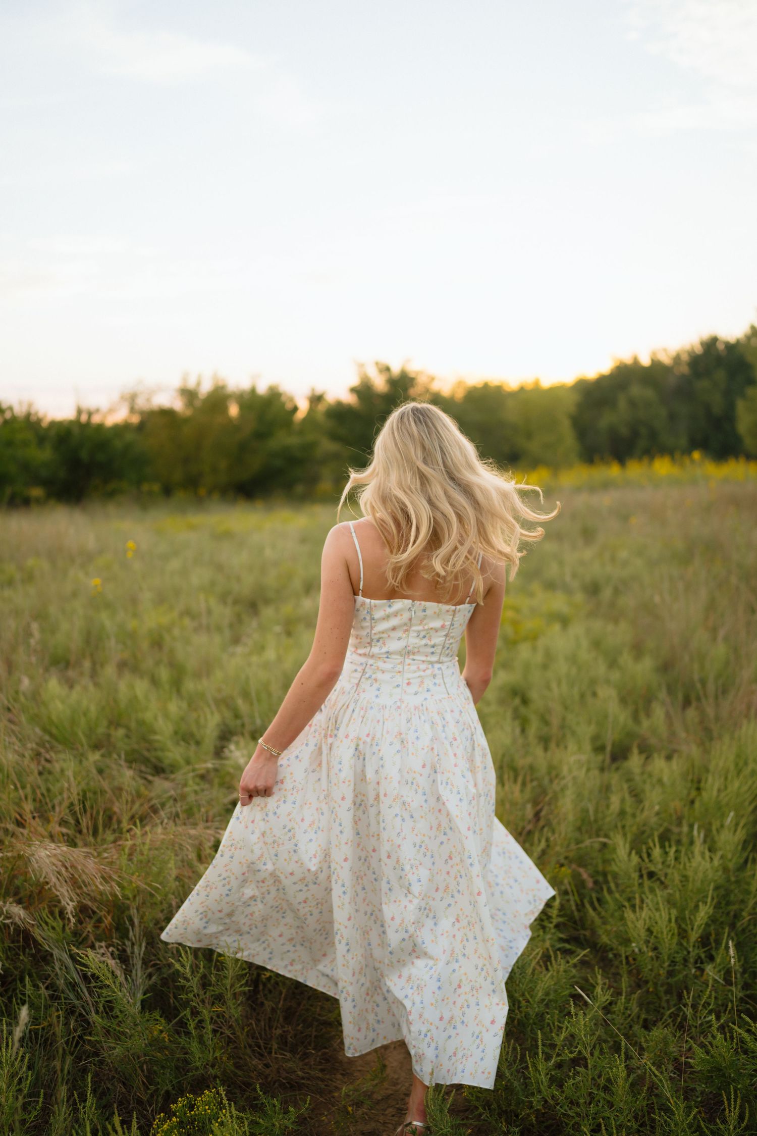 A white lace dress flows in the breeze as someone walks through a sunlit meadow.