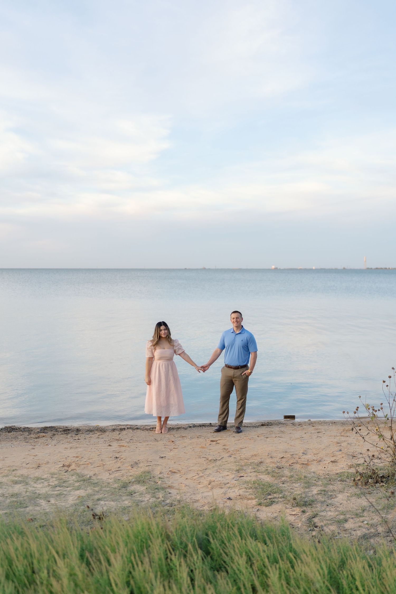 A couple walks along a serene beach at sunset holding hands in romantic silhouette against the water.