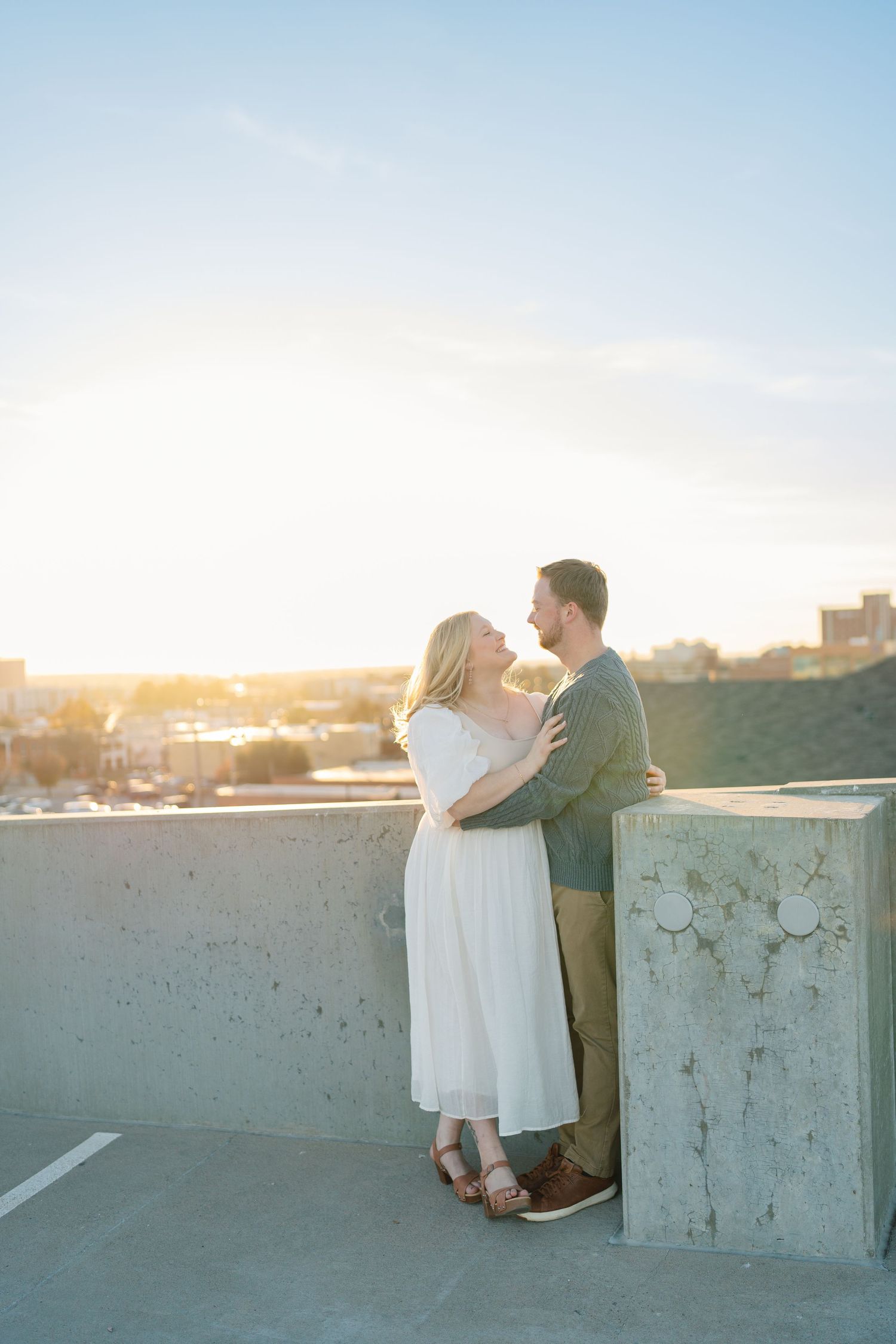 Couple embracing on rooftop during golden hour with urban backdrop.