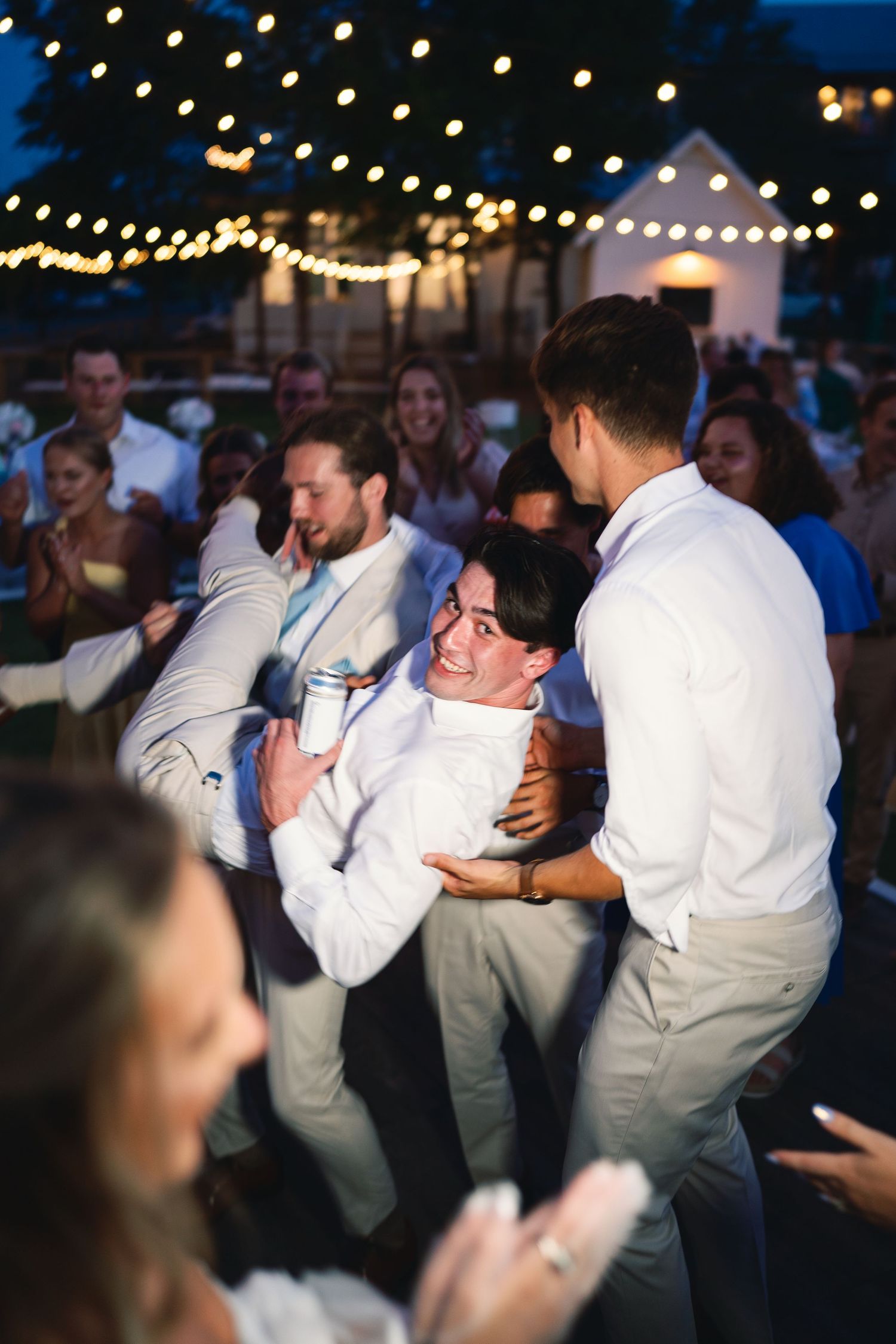 Wedding guests dancing under twinkling lights at an outdoor evening reception.